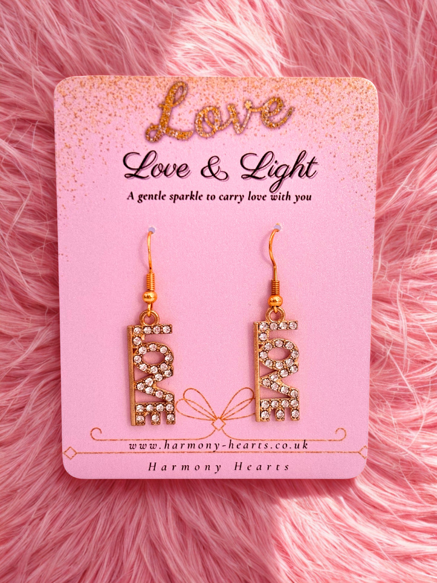 Gold sparkly earrings with the word love on a pink Harmony Hearts branded card