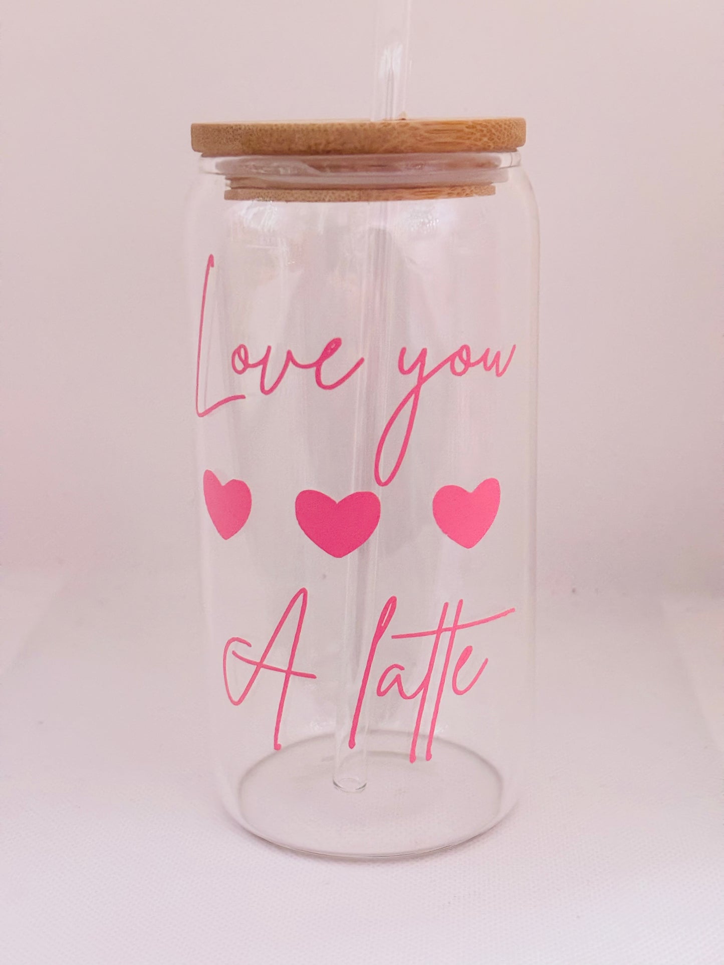 Clear glass tumbler with wooden lid, pink text 'Love you a latte' and hearts on a light pink background