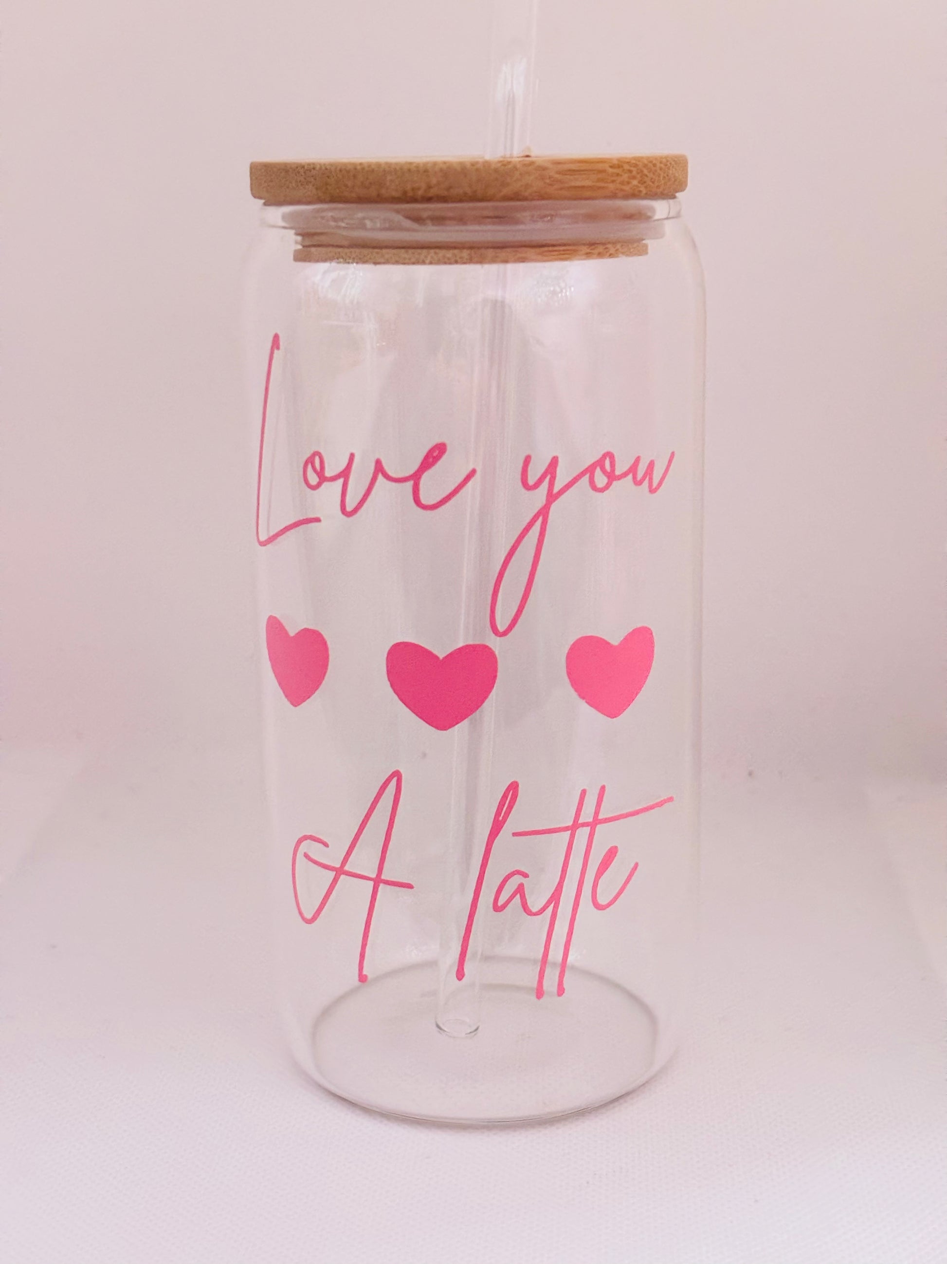 Clear glass tumbler with wooden lid, pink text 'Love you a latte' and hearts on a light pink background
