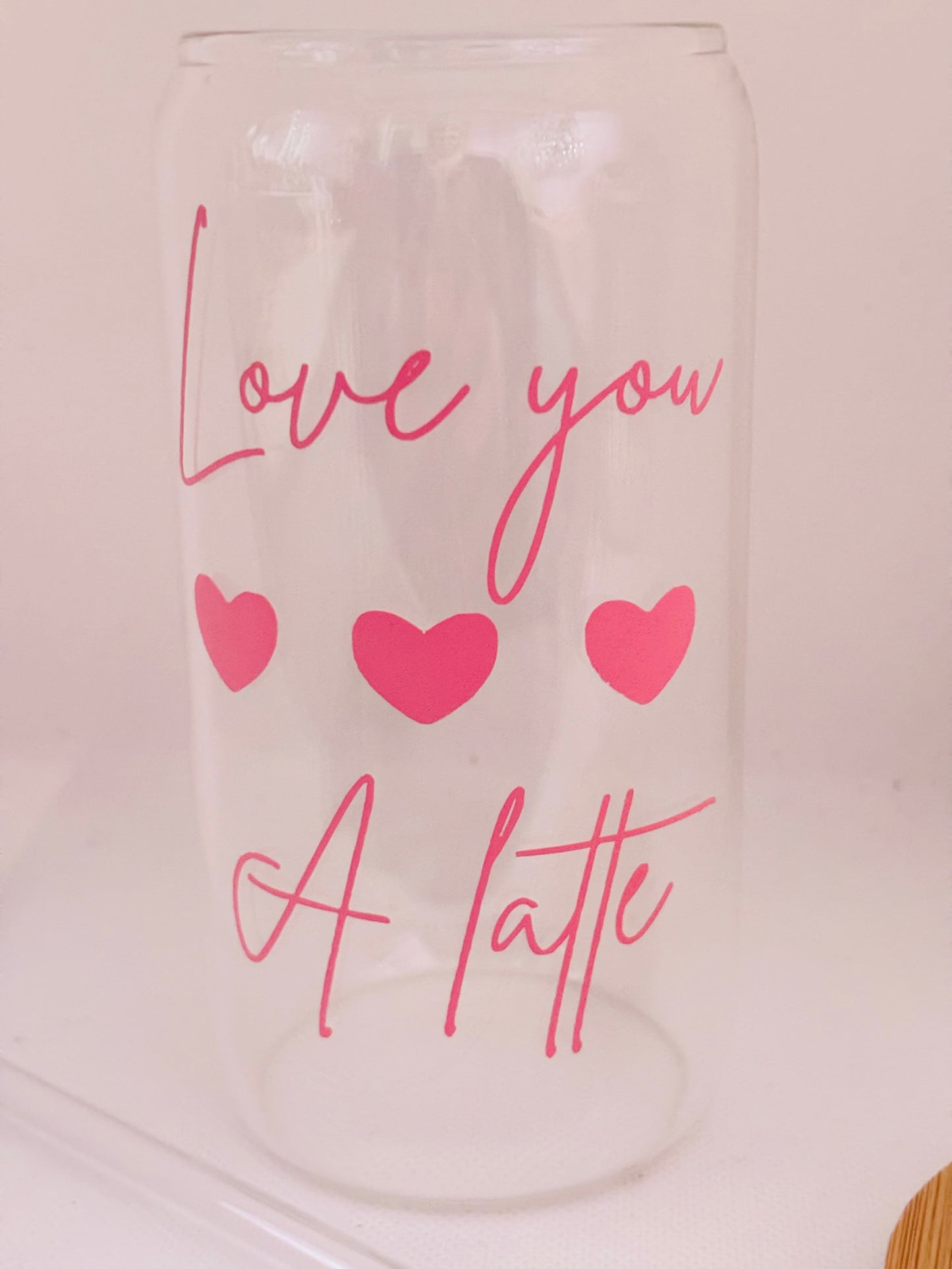 Clear glass tumbler with pink text 'Love you a latte' and hearts on a light pink background