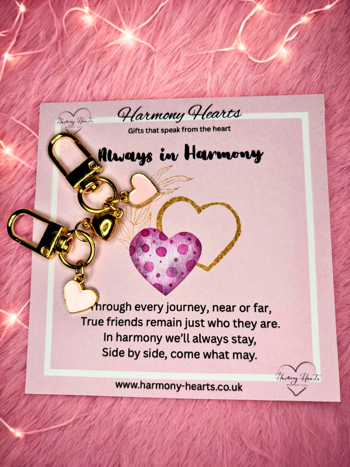 Heart-shaped keychain with gold accents on a pink card with text, against a pink textured background.
