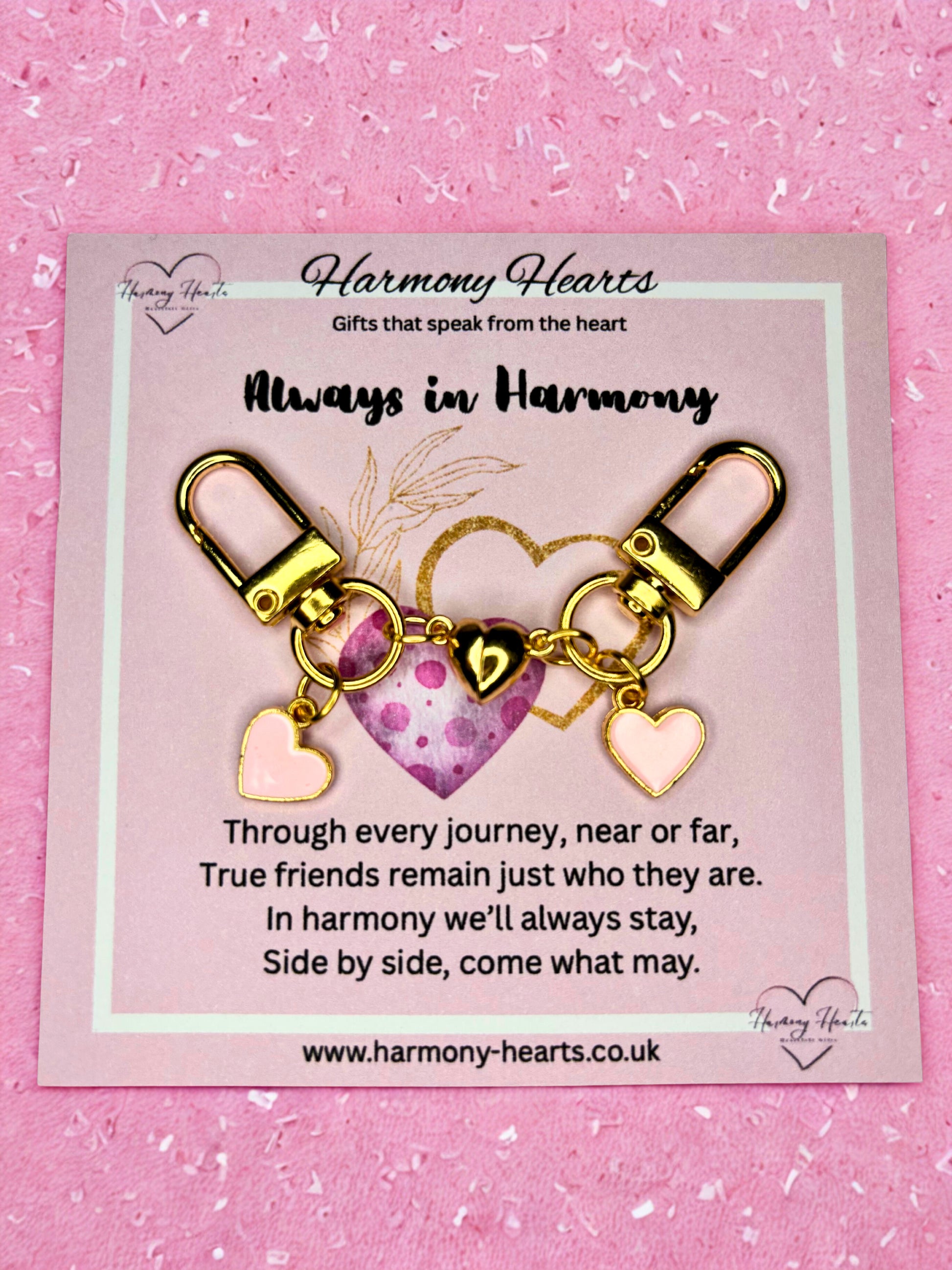Gold heart-shaped keychain with charms on a pink card with text, against a pink background.
