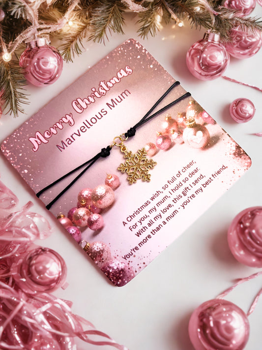 Pink Christmas card with gold snowflake charm bracelet surrounded by pink ornaments and tree branches.