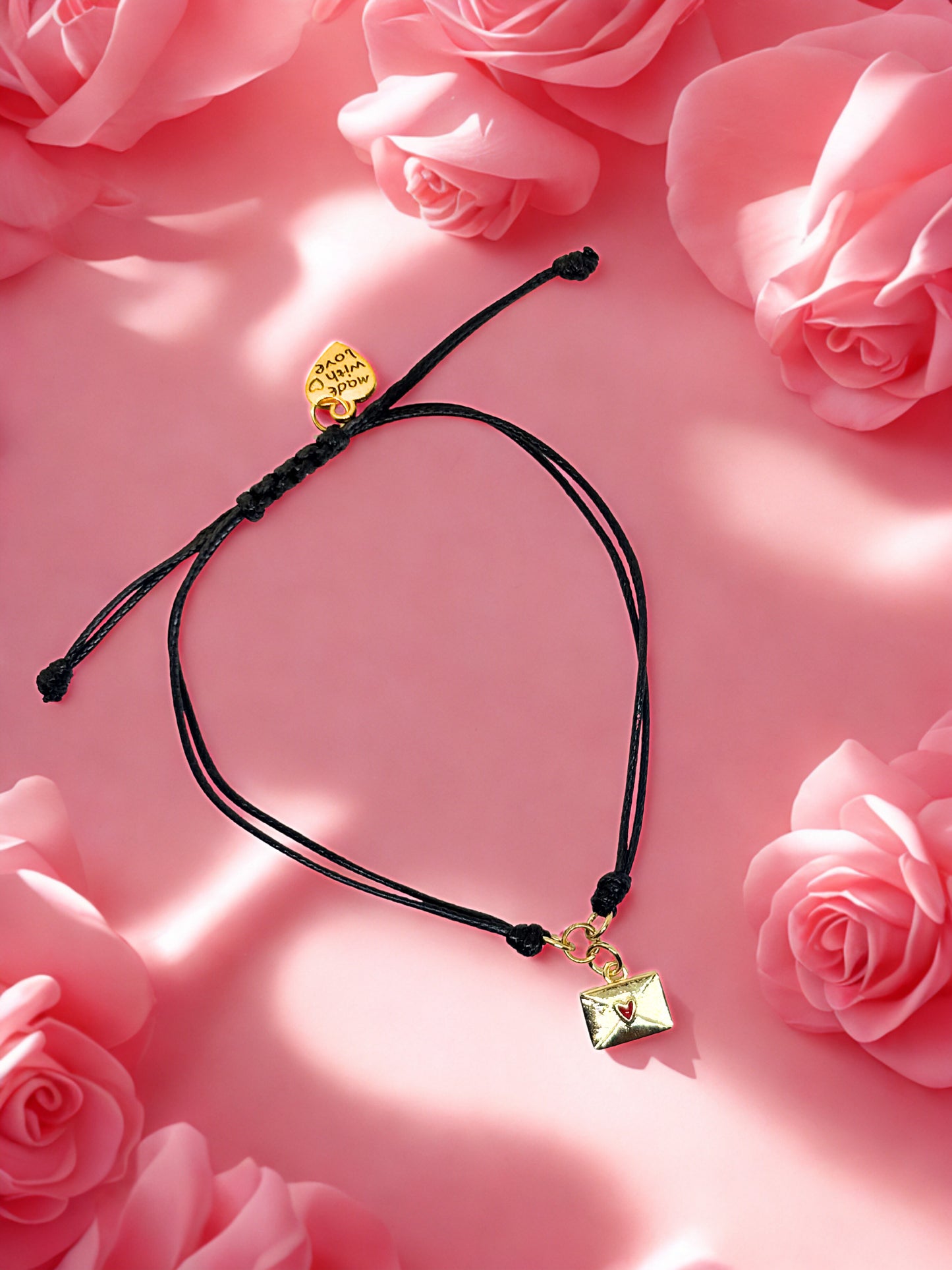Black cord bracelet with gold charm on a pink floral background