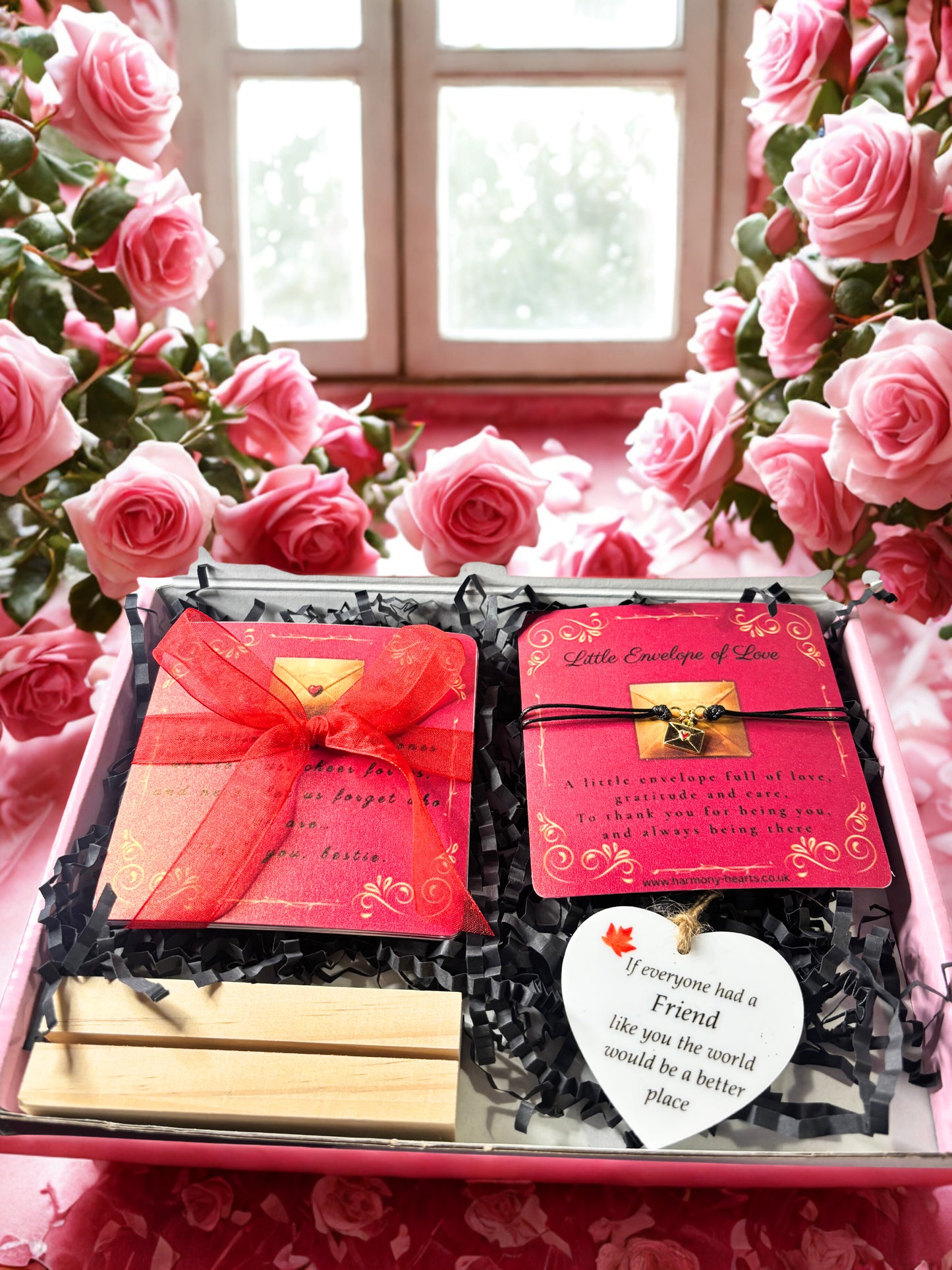 Gift set with red cards and wooden items, surrounded by pink roses.