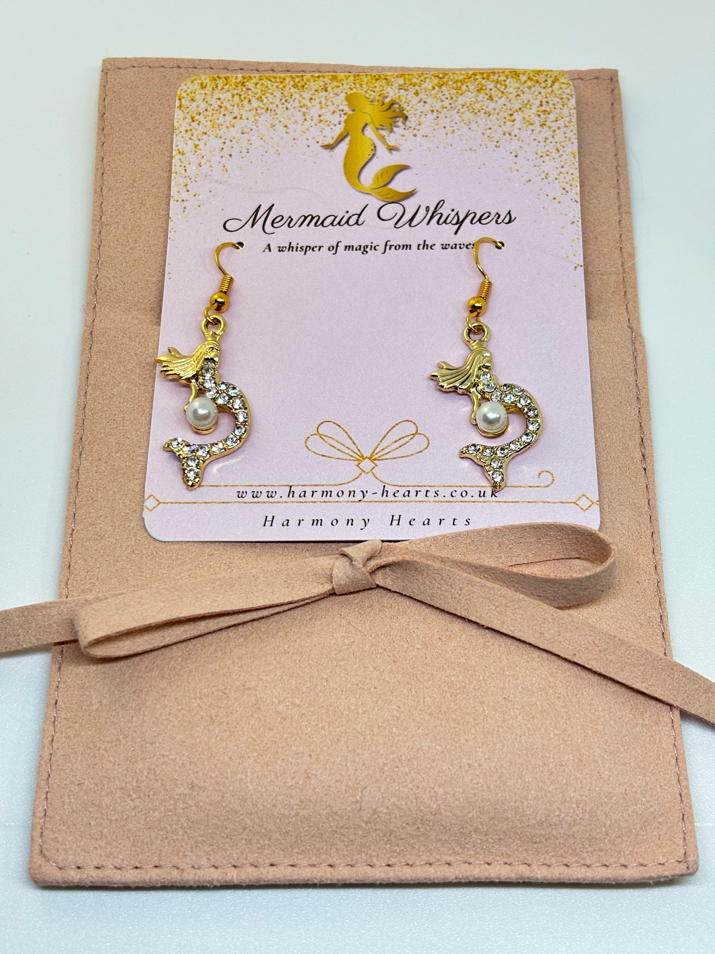 Pair of gold and pearl mermaid earrings on a 'Mermaid Whispers' card with a beige ribbon.