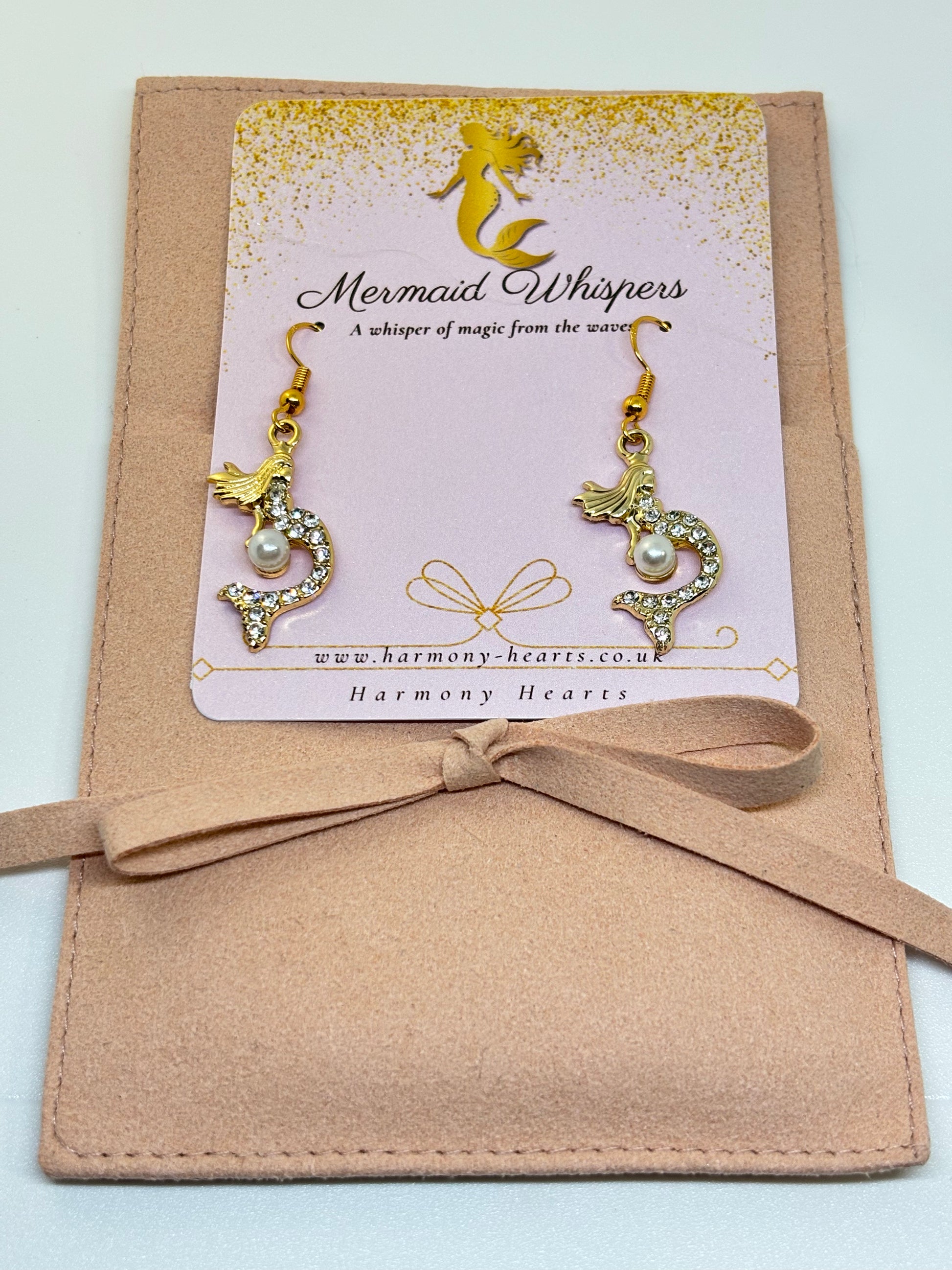 Pair of gold and pearl mermaid earrings on a 'Mermaid Whispers' card with a beige ribbon.