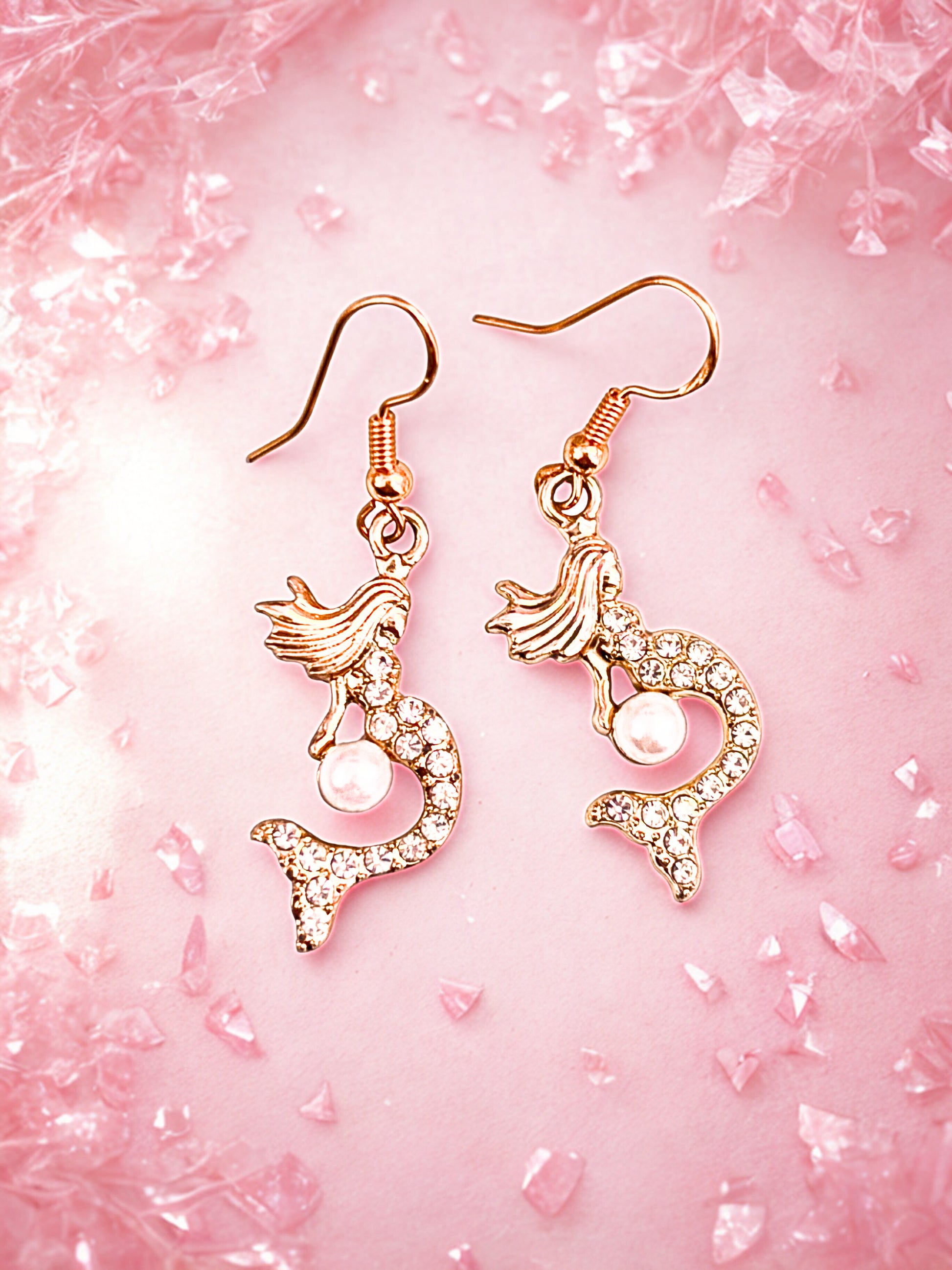 Mermaid-shaped earrings on a pink textured background