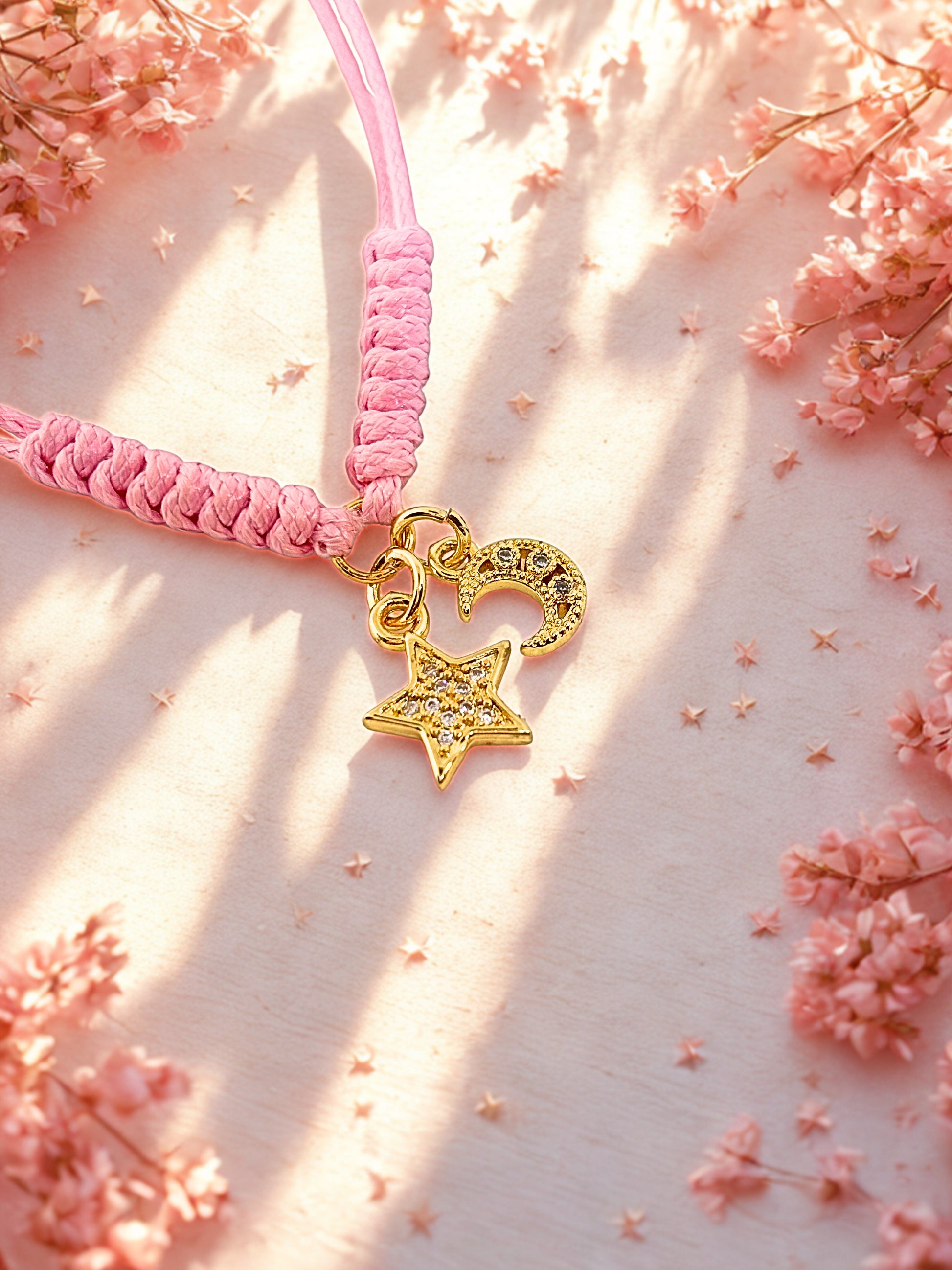 Pink bracelet with gold charm featuring a star and a moon on a soft pink background with flowers.