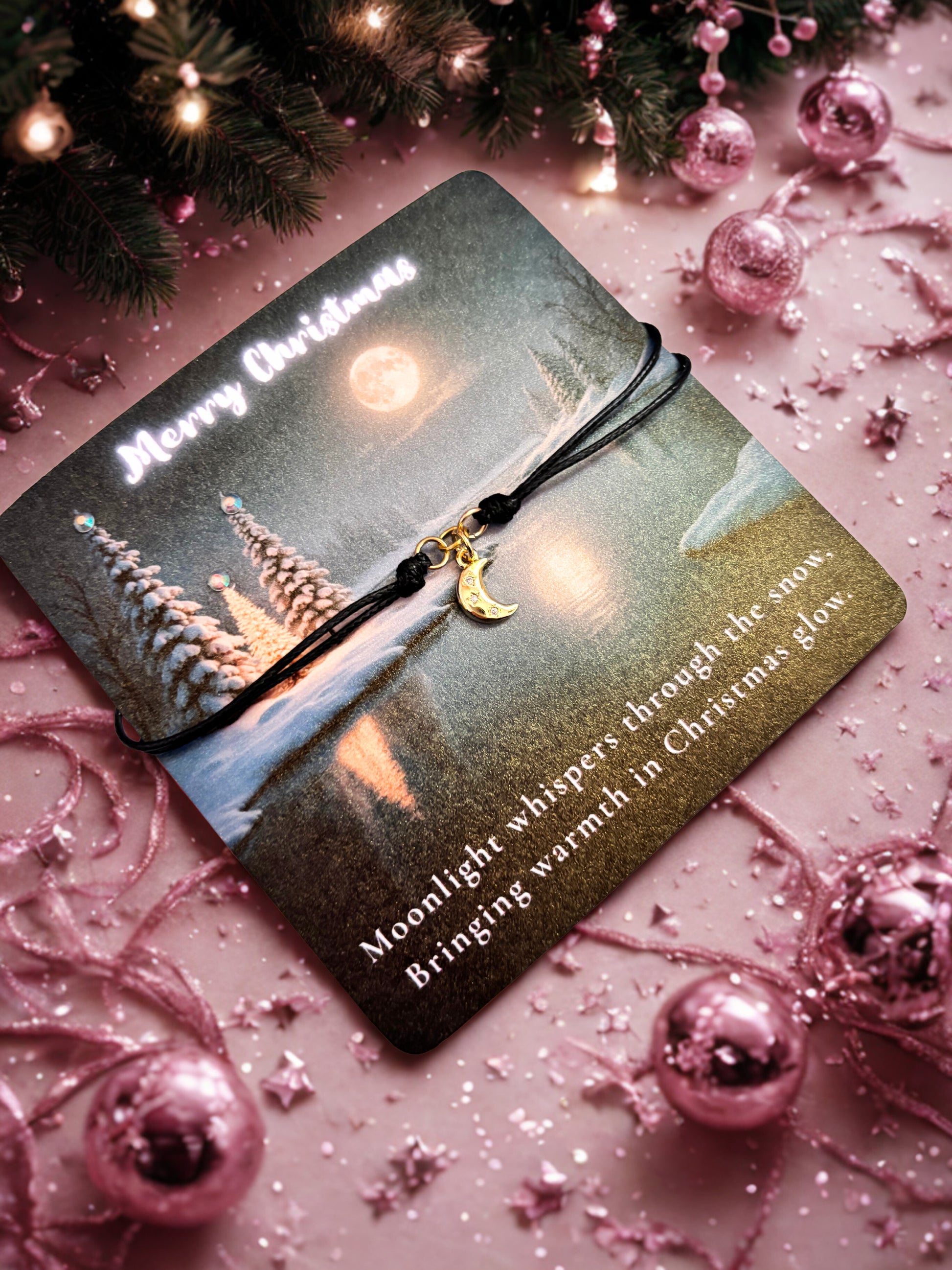 Gold moon charm on a decorative card with a Christmas theme on a pink background with ornaments