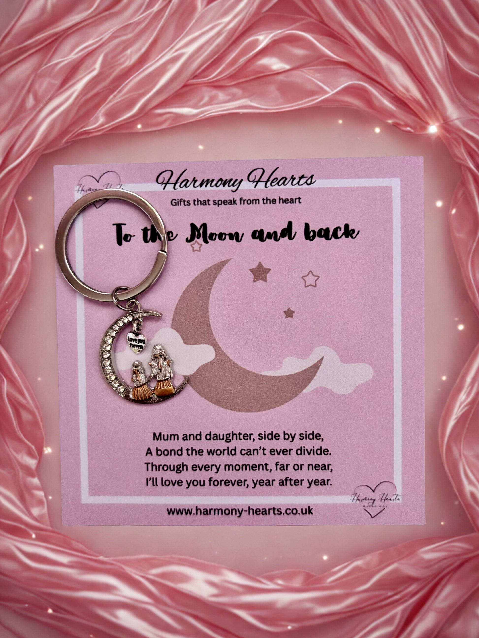 Keychain with moon and star design on a pink card with text, against a pink fabric background.