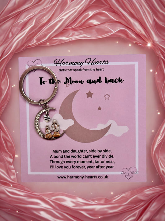 Keychain with moon and star design on a pink card with text, against a pink fabric background.