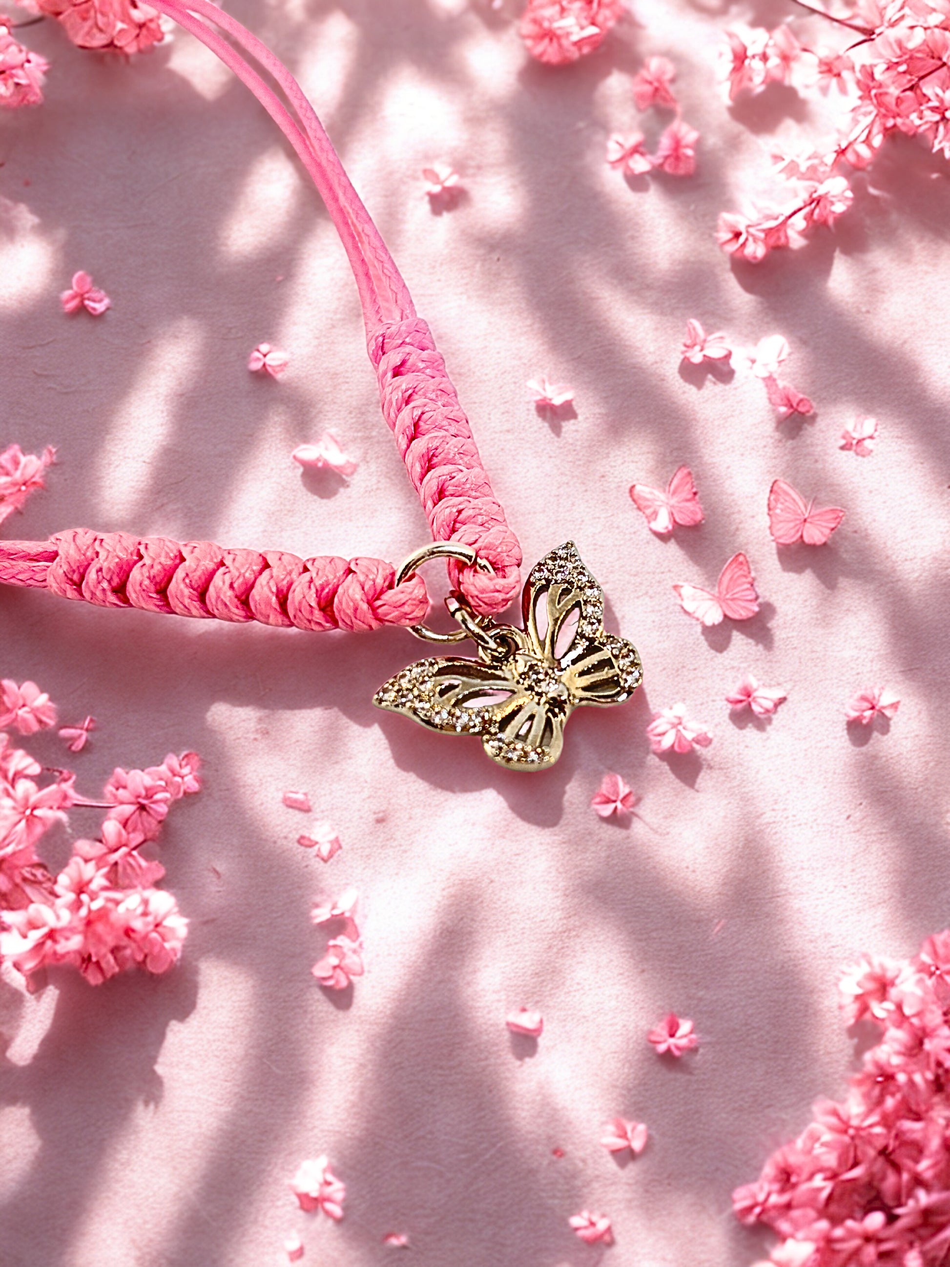 Pink braided bracelet with a silver butterfly charm on a pink floral background