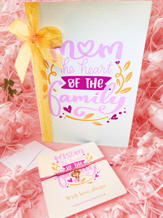 Greeting card with 'Mom, the heart of the family' text with a matching gold heart charm bracelet on a pink background