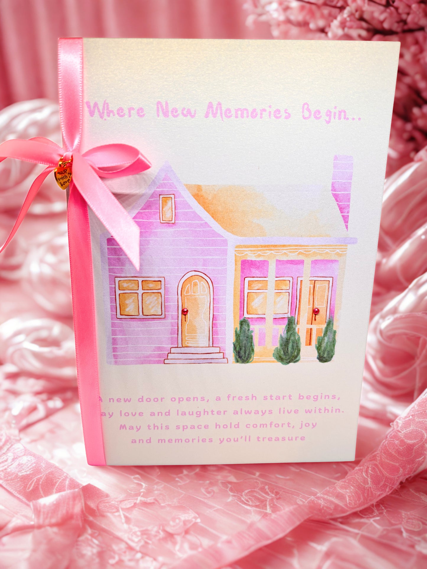 Greeting Card New Home with a house illustration and pink ribbon on a pink fabric background