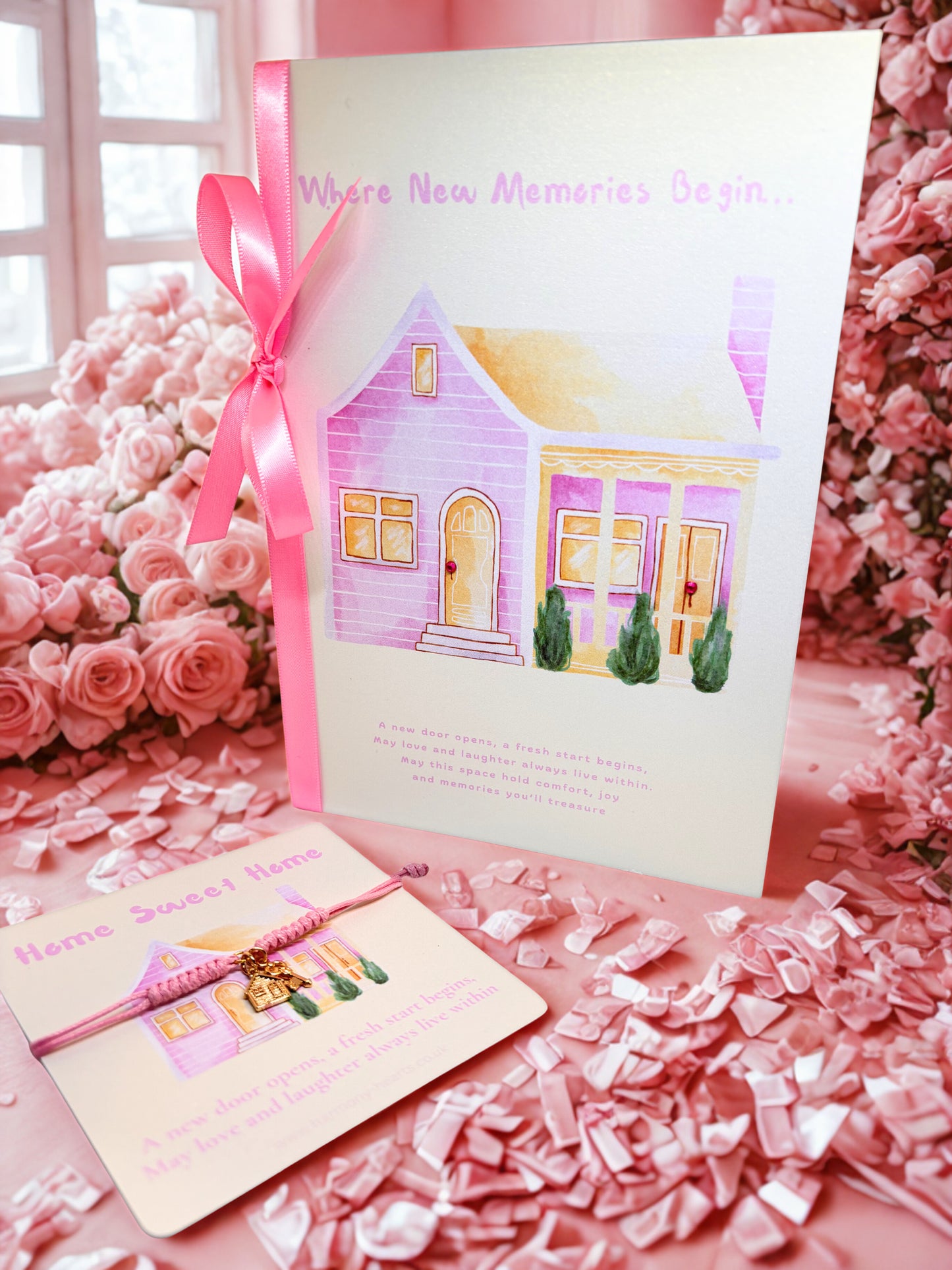 Pink house-themed new home card with a pink ribbon and a pink cord charm bracelet on s matching backing card on a pink floral background 