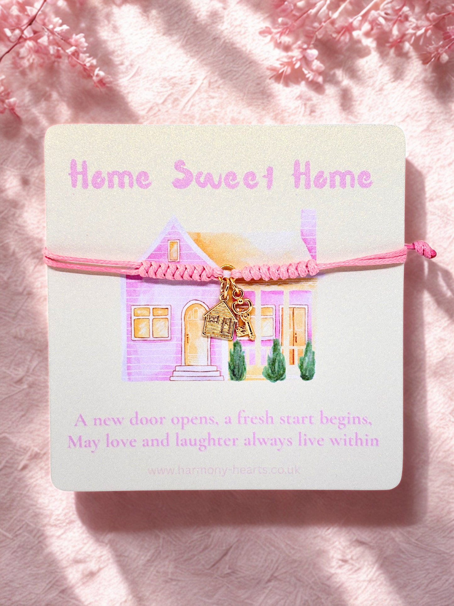 Pink cord bracelet on a decorative card with a house illustration and 'Home Sweet Home' text on a pink background.