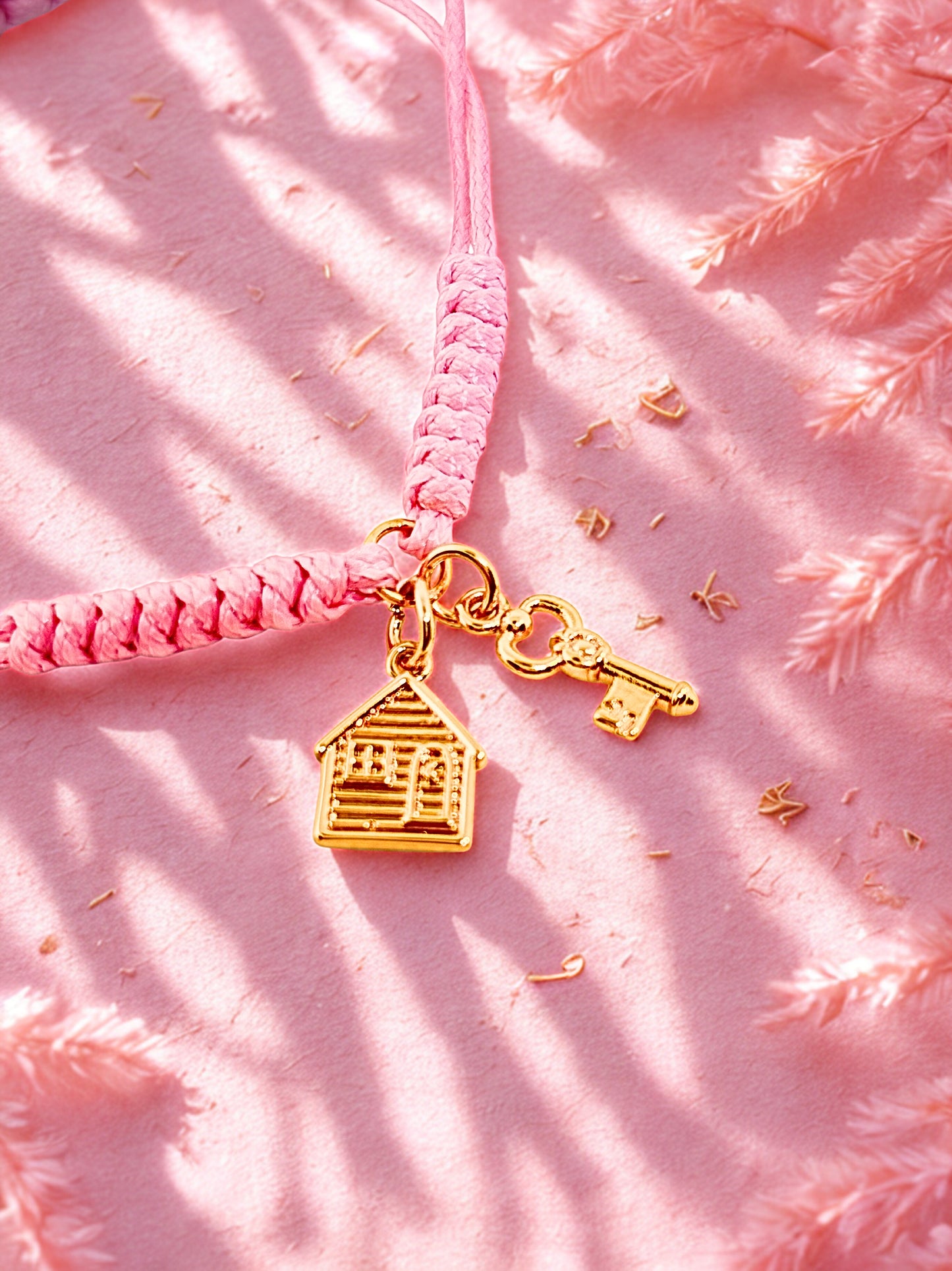Pink cord bracelet vwith gold house and key charm on a pink textured background