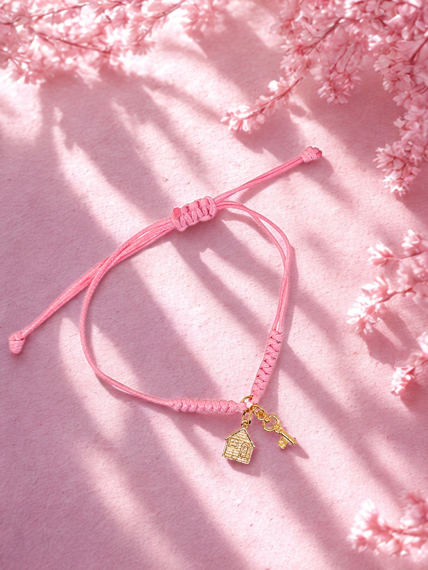 Pink bracelet with gold house and key charms on a pink floral background