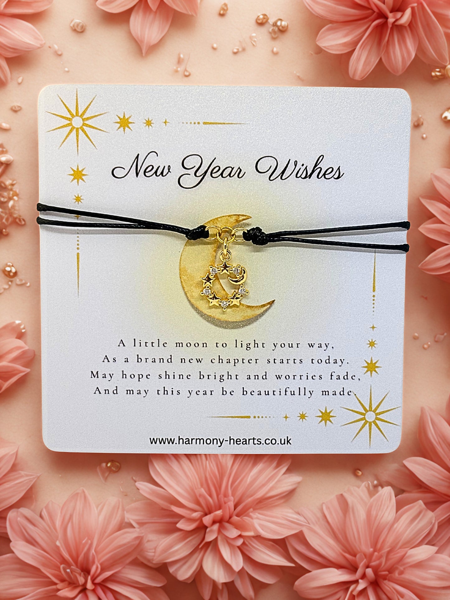 Bracelet with moon charm on a 'New Year Wishes' card surrounded by pink flowers.
