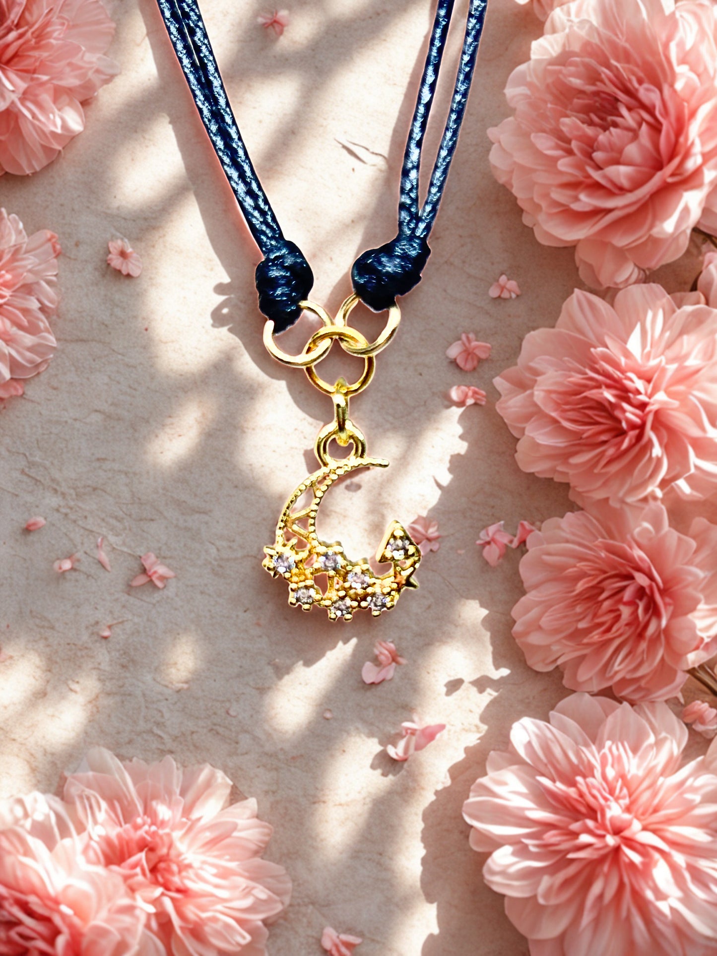 Gold crescent moon bracelet with black cord on a pink floral background