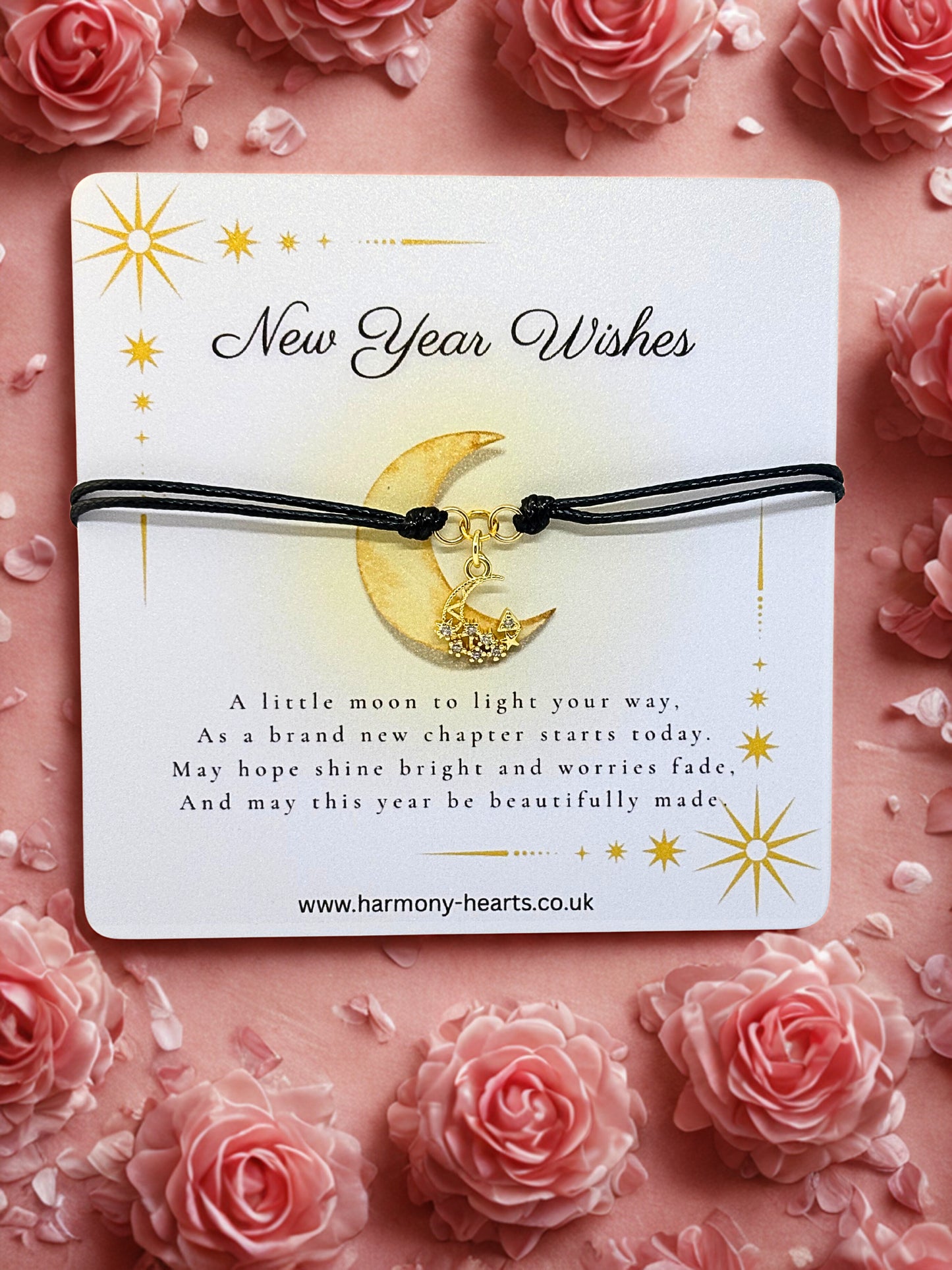 Bracelet with moon charm on a 'New Year Wishes' card surrounded by pink roses.