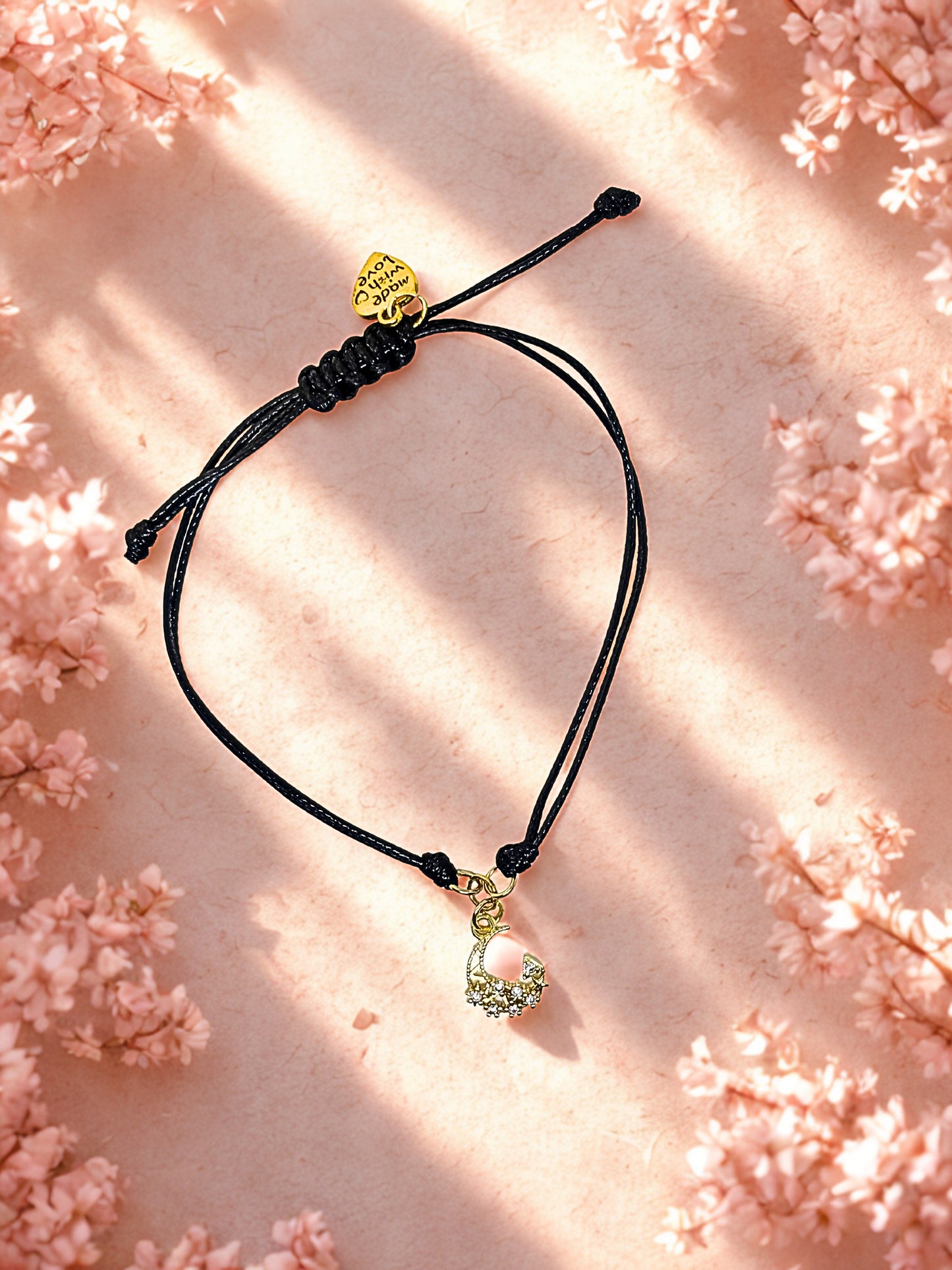 Bracelet with gold moon charm on a pink floral background