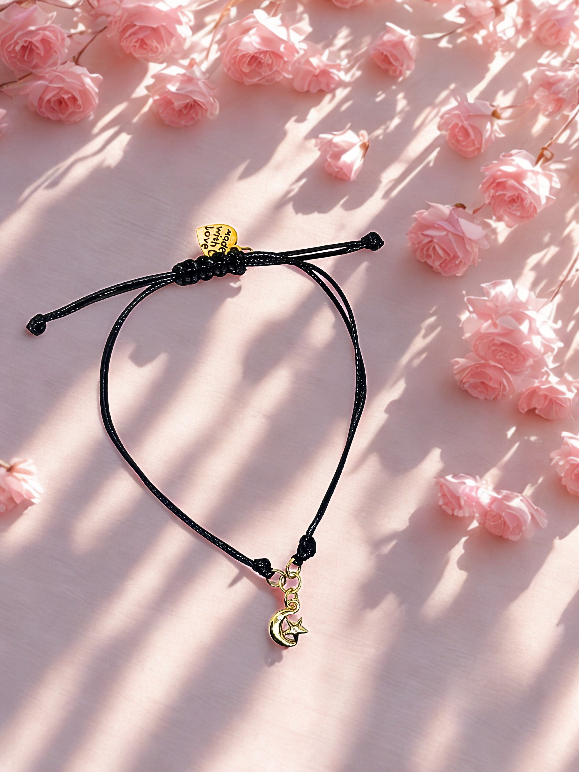 Black cord bracelet with gold moon charm on a pink floral background