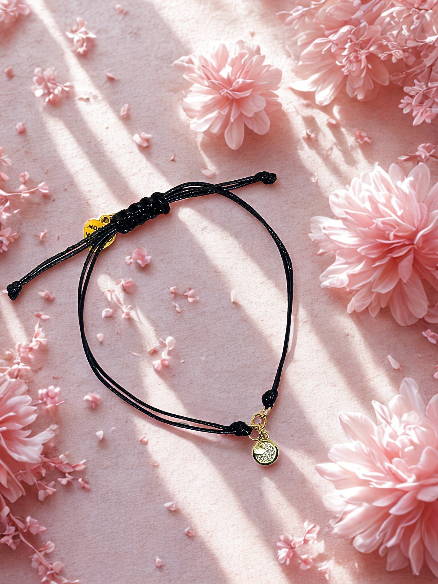 Black cord bracelet with gold moon charm on a pink floral background