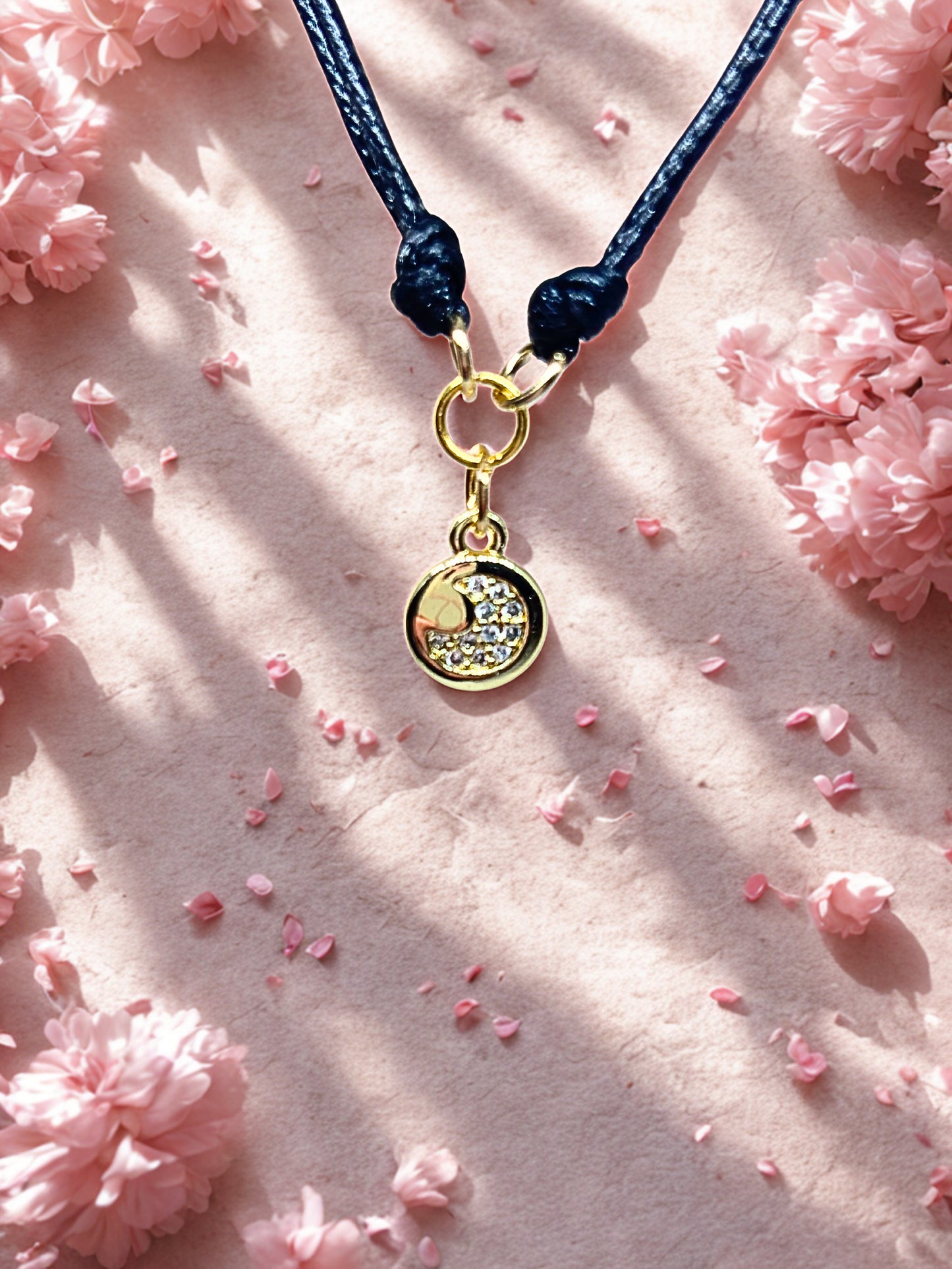 Bracelet with a gold moon charm on a pink floral background