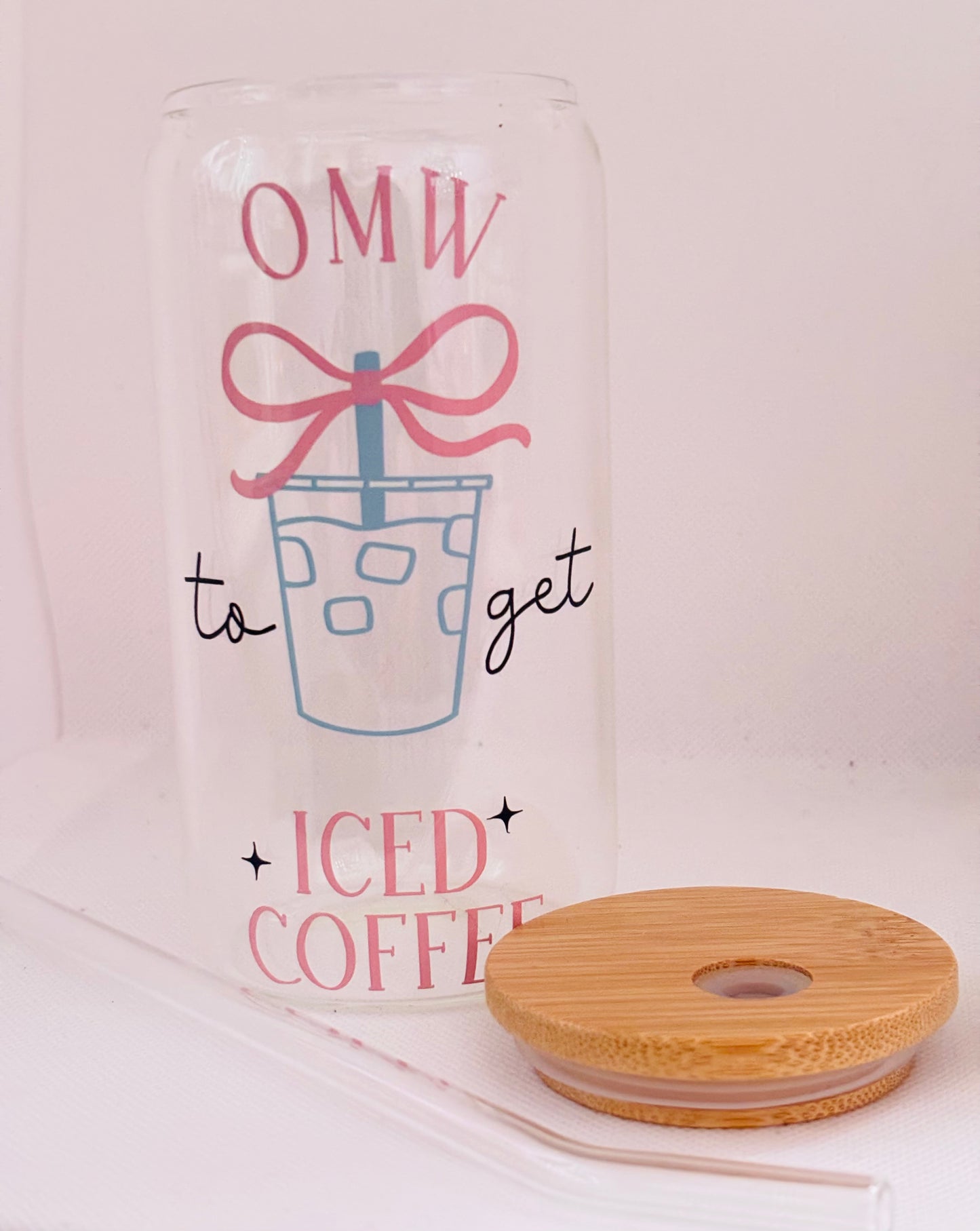 Clear tumbler with 'OMW to get iced coffee' text and a pink bow, next to a wooden diffuser on a light pink background.