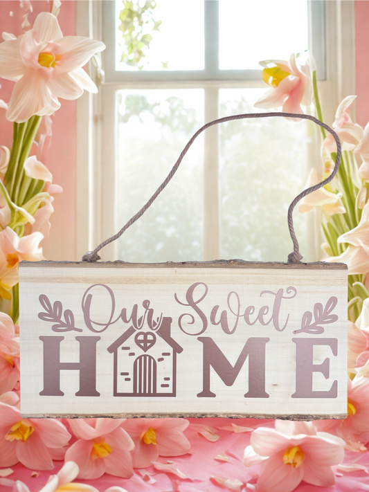 Decorative sign with 'Our Sweet Home' text hanging in front of a window with pink floral decorations.