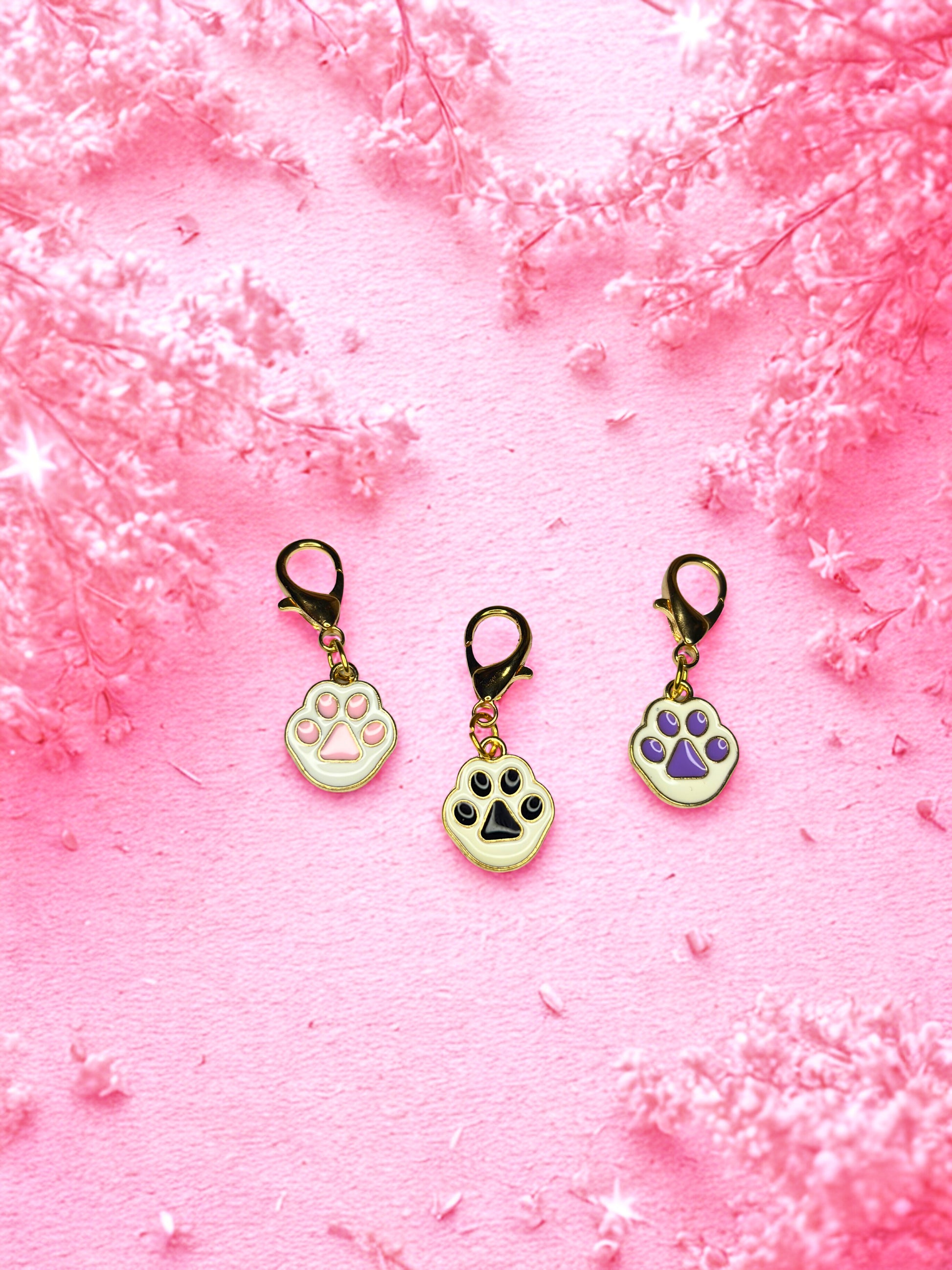 Three paw-shaped keychains on a pink textured background