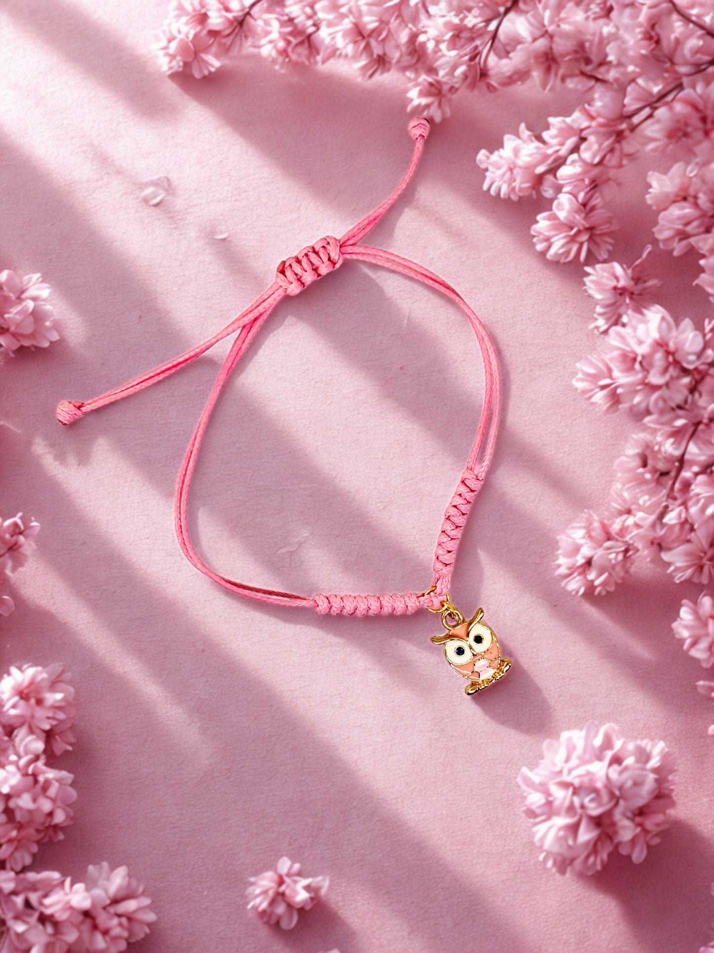Pink cord bracelet with an owl charm on a pink background