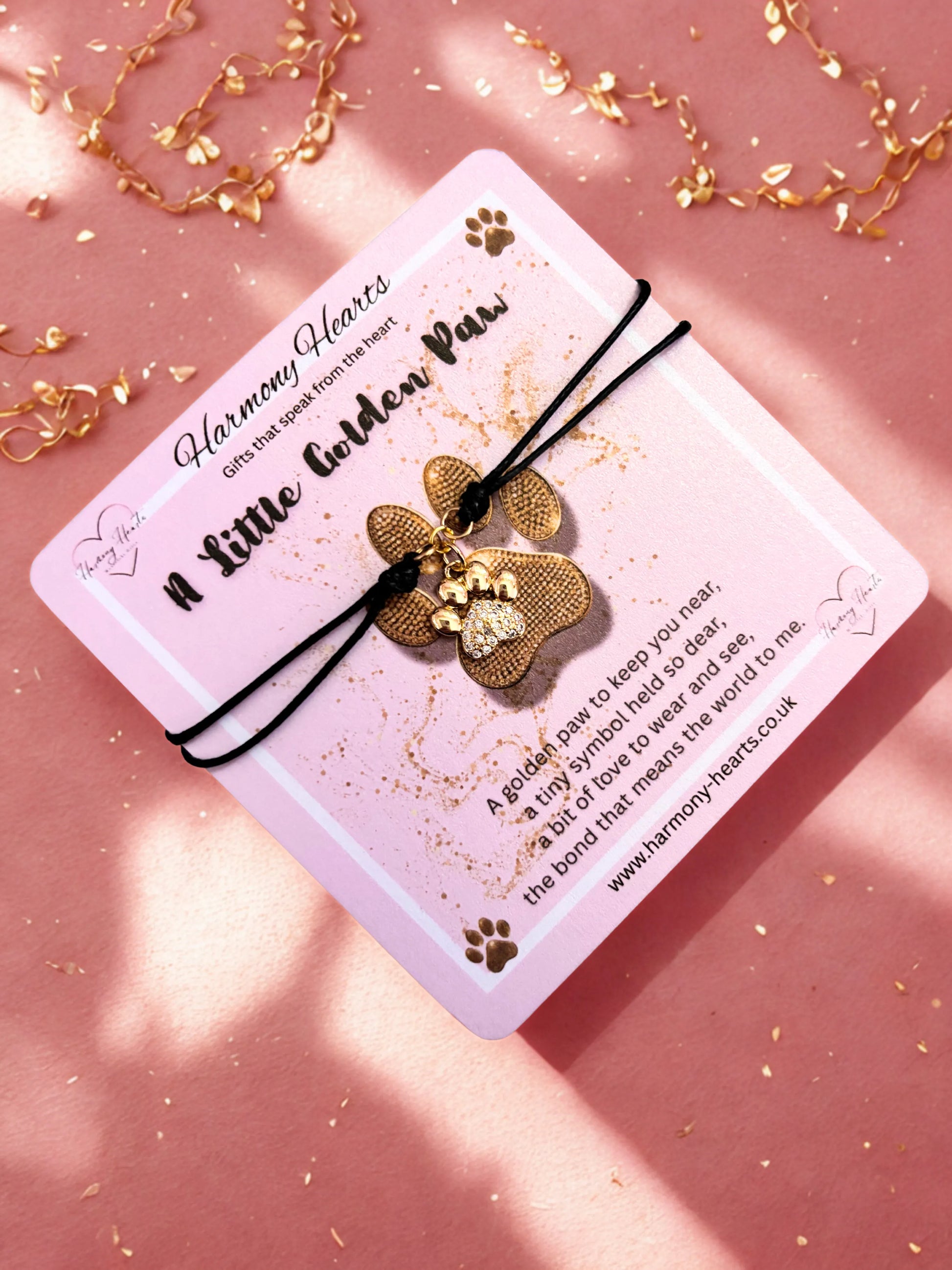 Gold paw-shaped charm bracelet on a card with text on a pink background