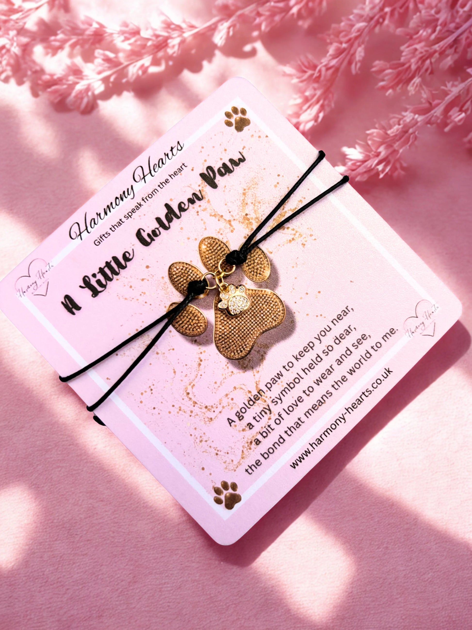 Gold paw-shaped charm bracelet on a card with text on a pink background