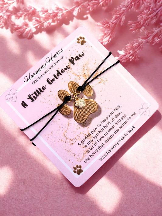 Gold paw-shaped charm bracelet on a card with text on a pink background