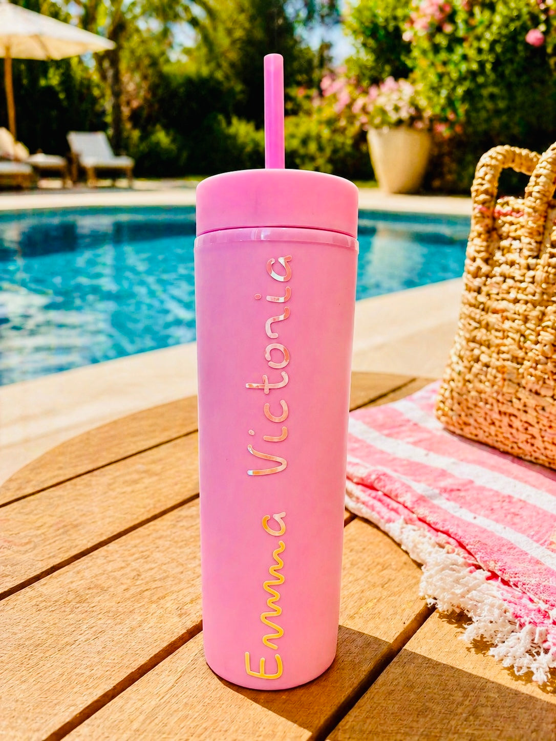Pink personalised tumbler with straw on a wooden deck by a poolside
