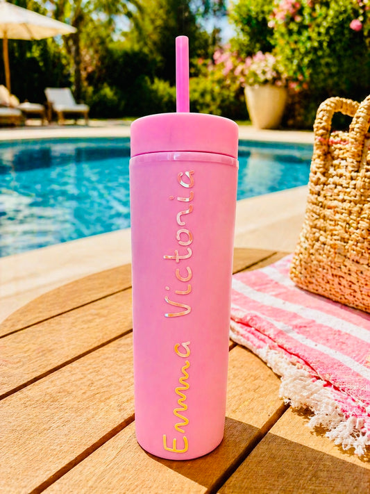 Pink personalised tumbler with straw on a wooden deck by a poolside