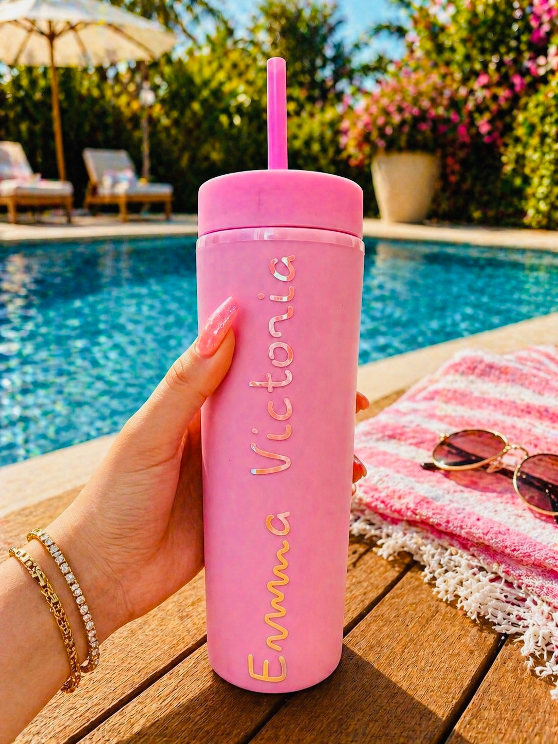 Pink tumbler with straw held by a hand by a poolside