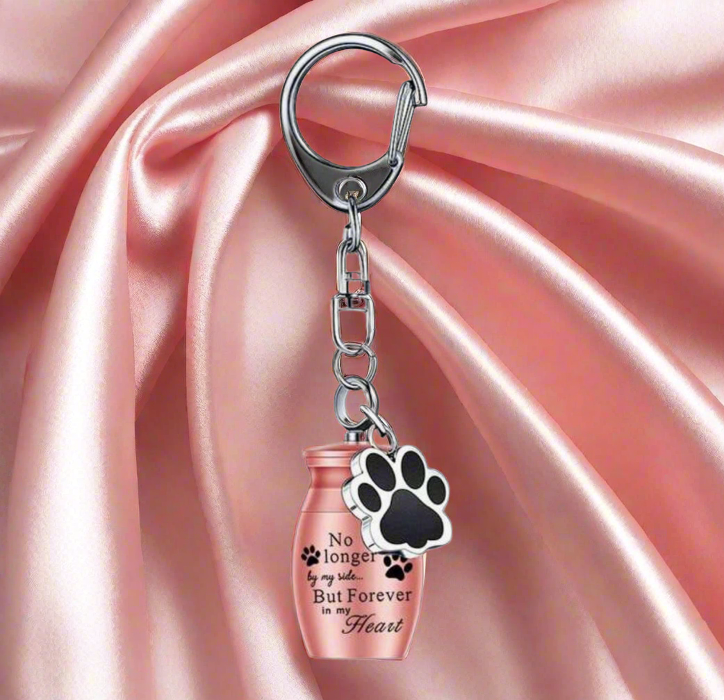 Keychain with paw print and pink urn on pink satin background