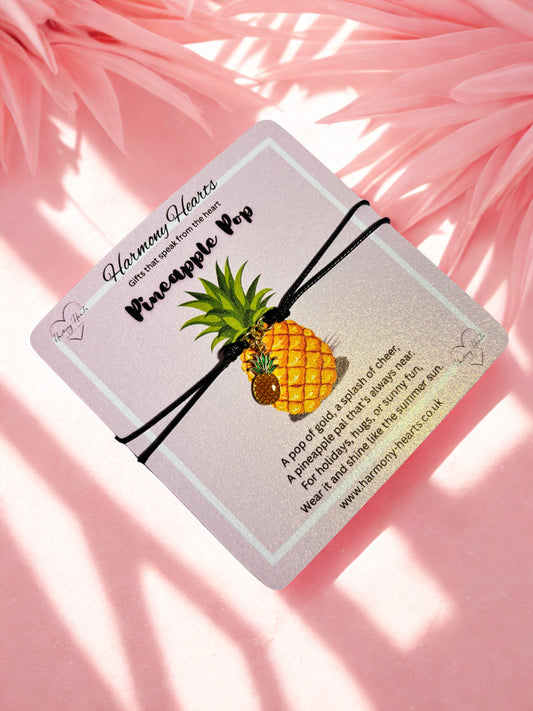 Black cord bracelet with a pineapple charm on a pink poem card on a pink background