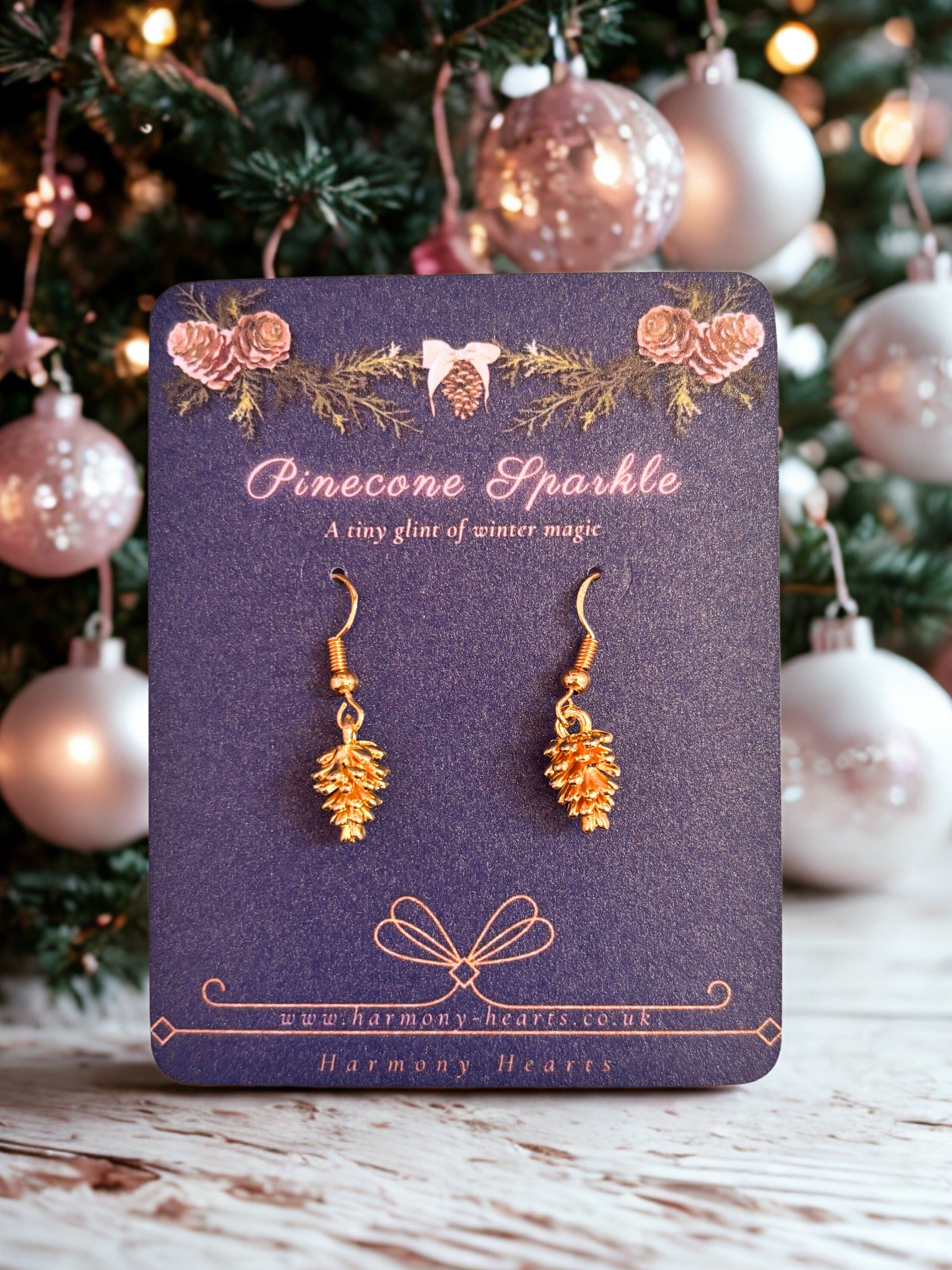 Pinecone-shaped earrings on a purple card with Christmas tree in the background