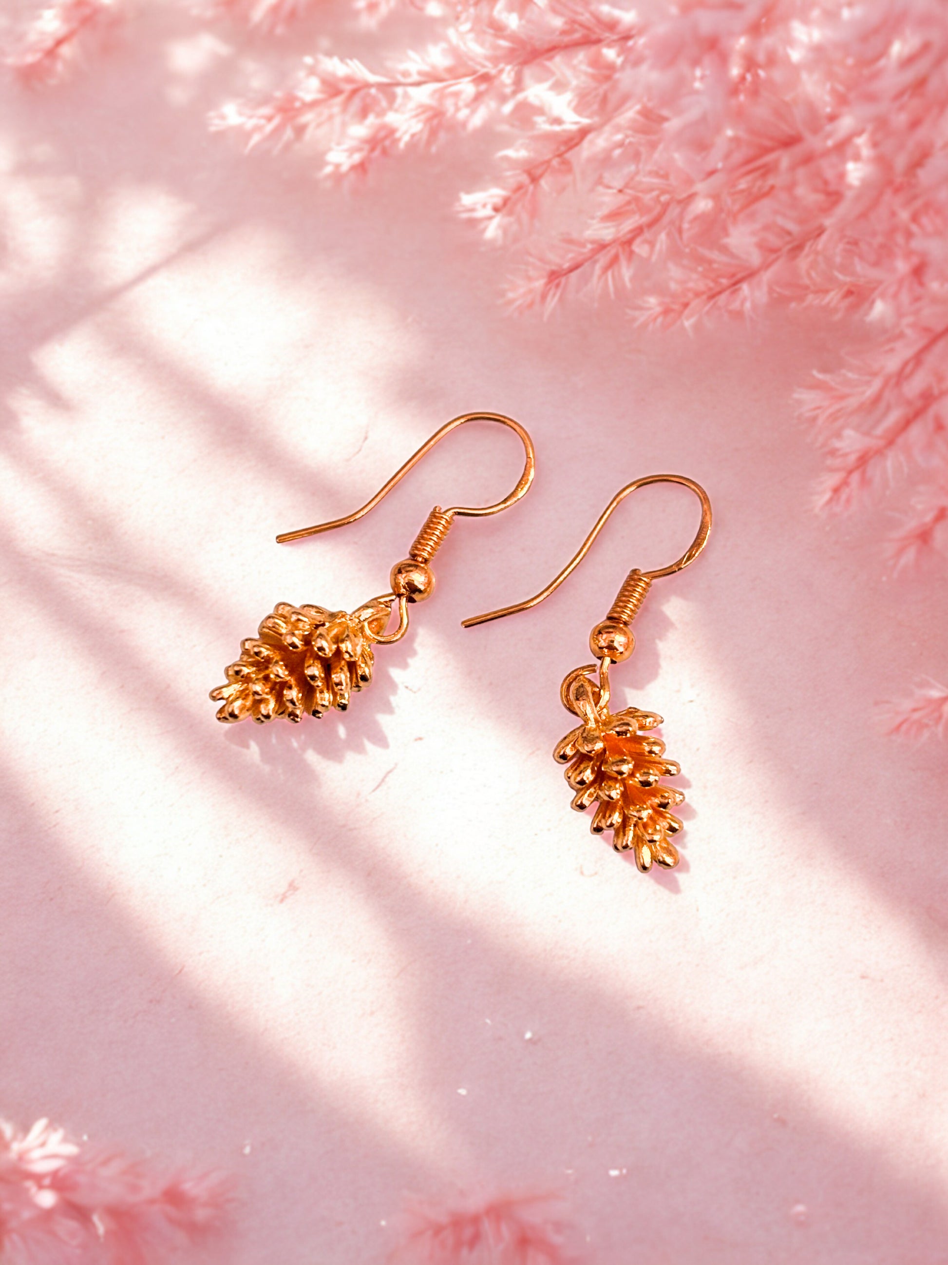 Gold pinecone shaped earrings on a pink textured background