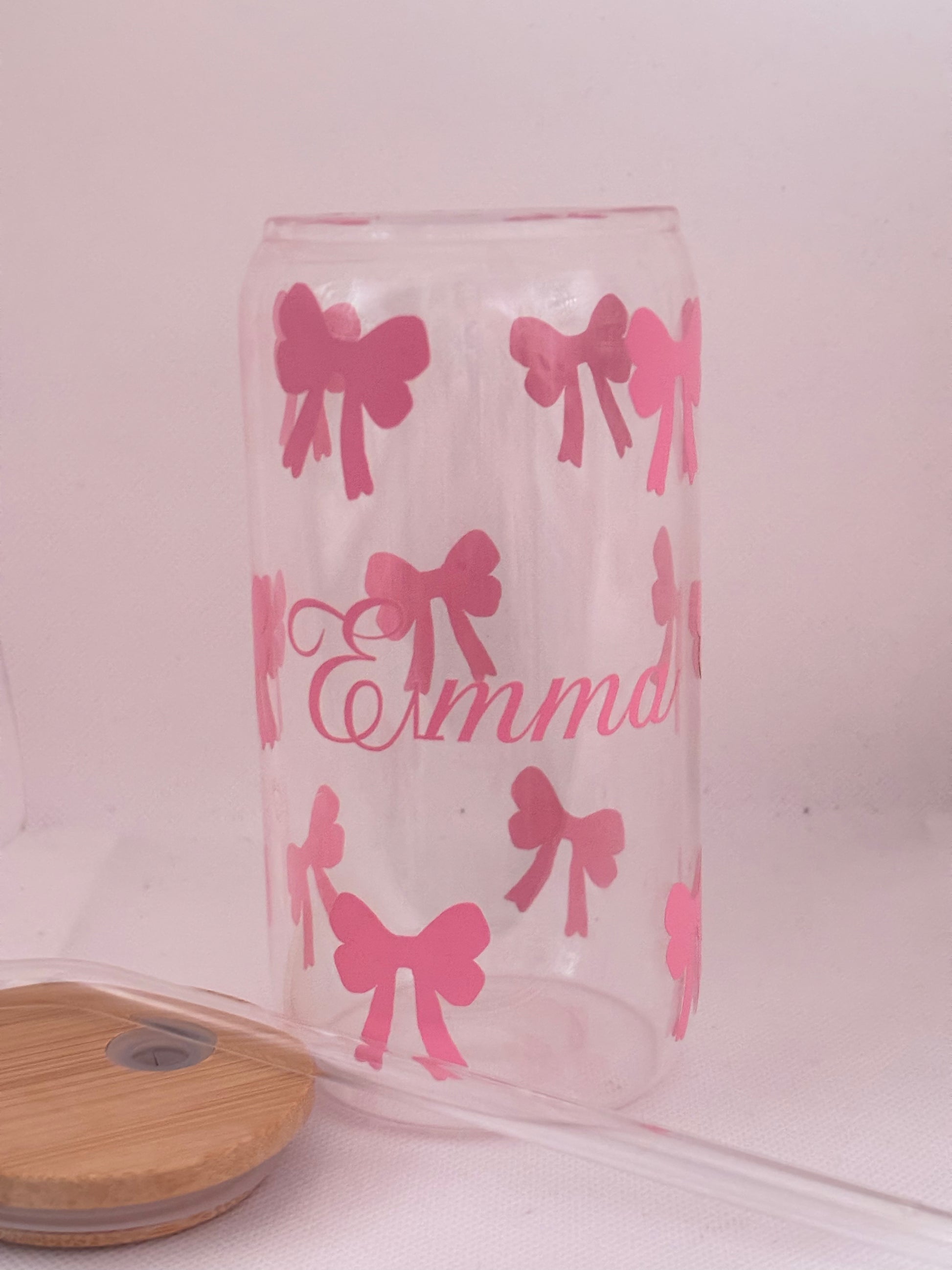 Clear glass tumbler with pink bow patterns and 'Emma' text on a white background