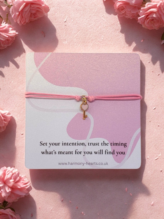 Pink bracelet with a key charm on a card with floral background