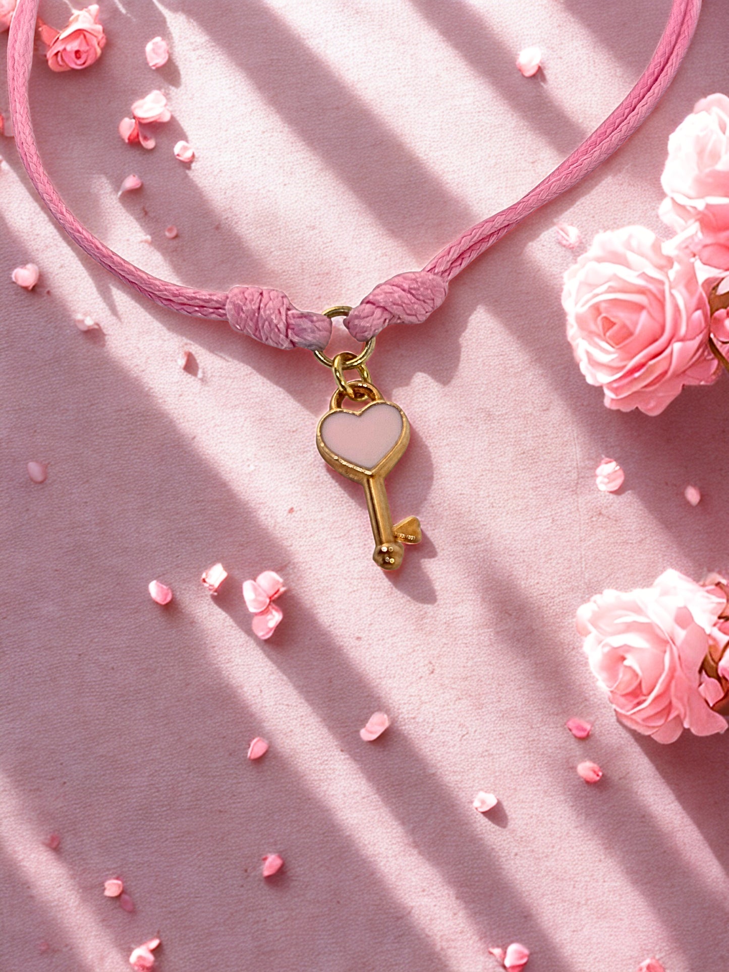 Pink cord bracelet with a gold key-shaped charm on a pink background with flowers.