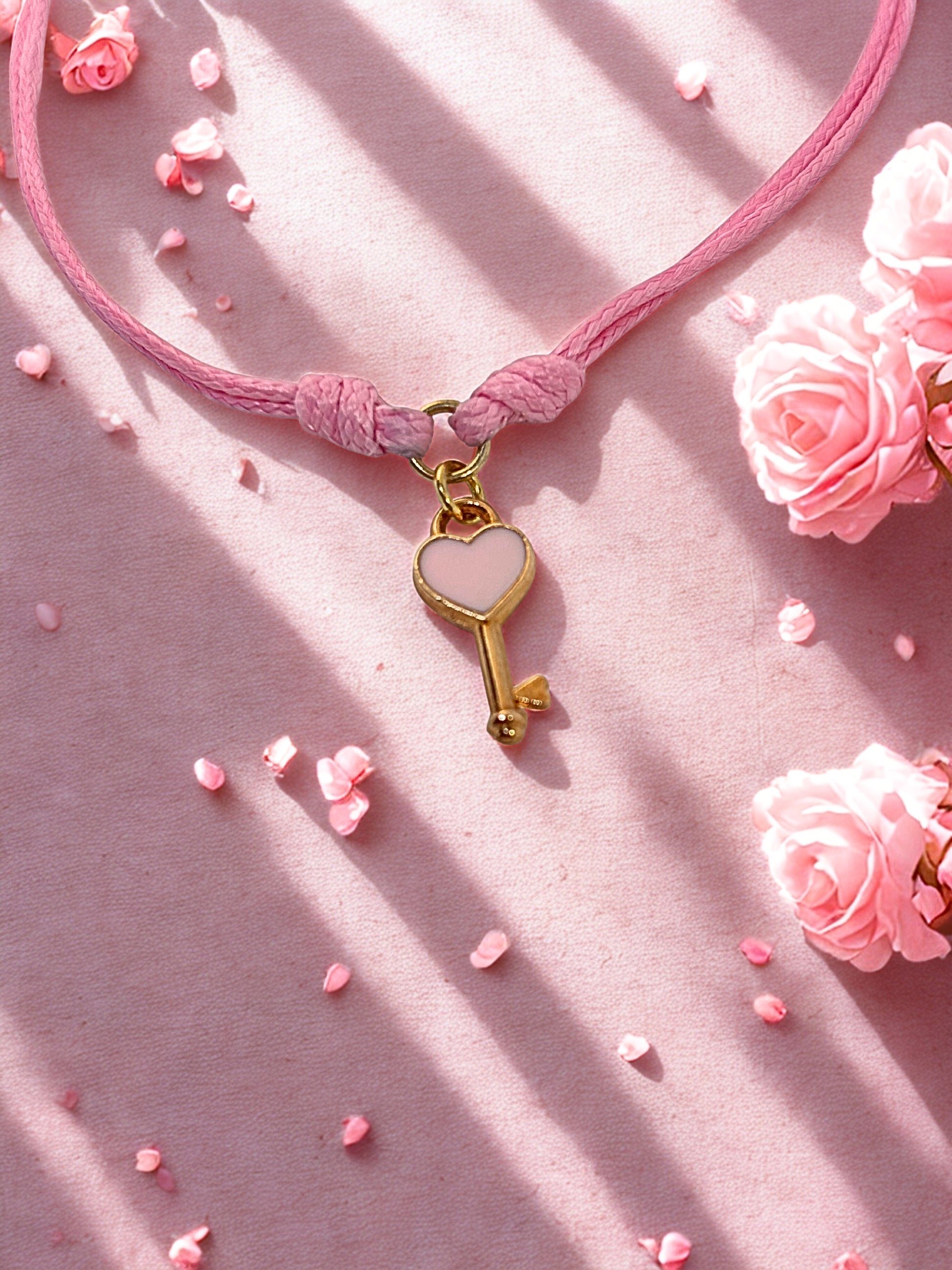 Pink cord bracelet with a gold key-shaped charm on a pink background with flowers.