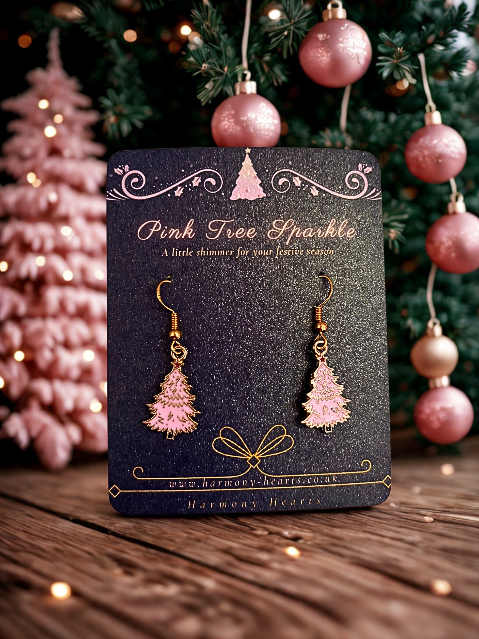 Pink tree-shaped earrings on a card with Christmas decorations in the background