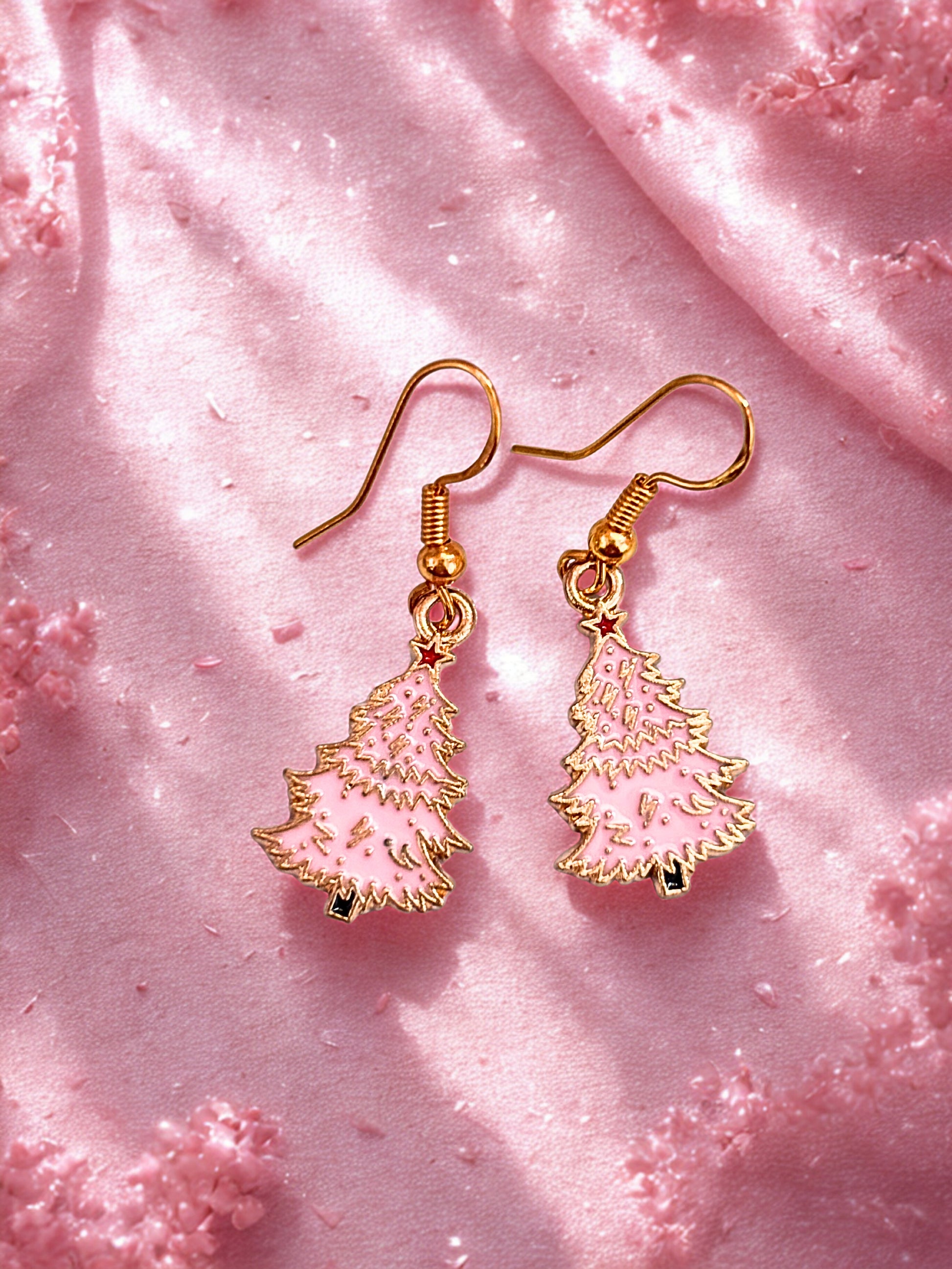 Gold and pink Christmas tree earrings on a pink textured fabric background